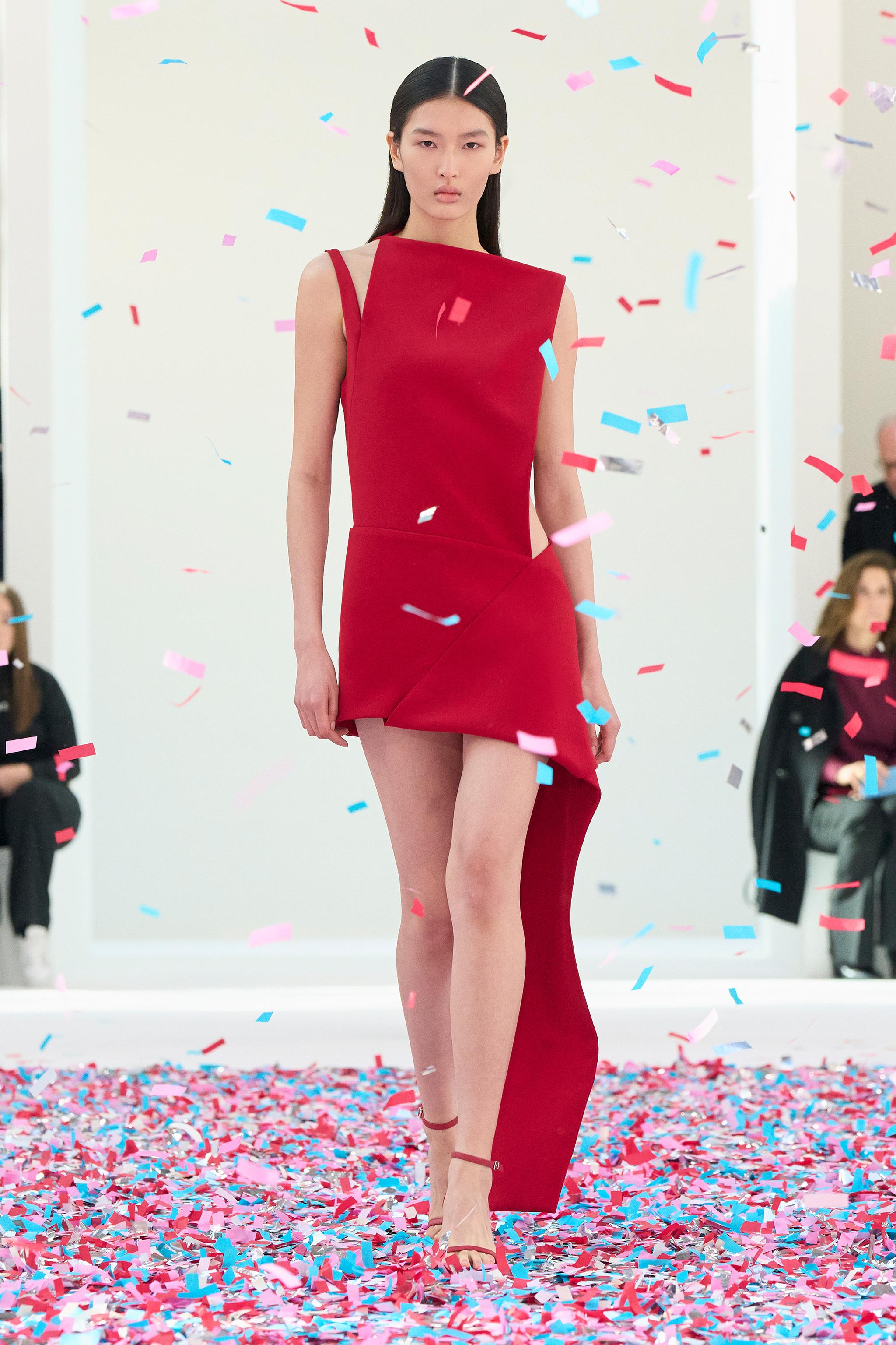 Elegant red Courrèges dress showcased on a runway with colorful confetti at an fashion event.