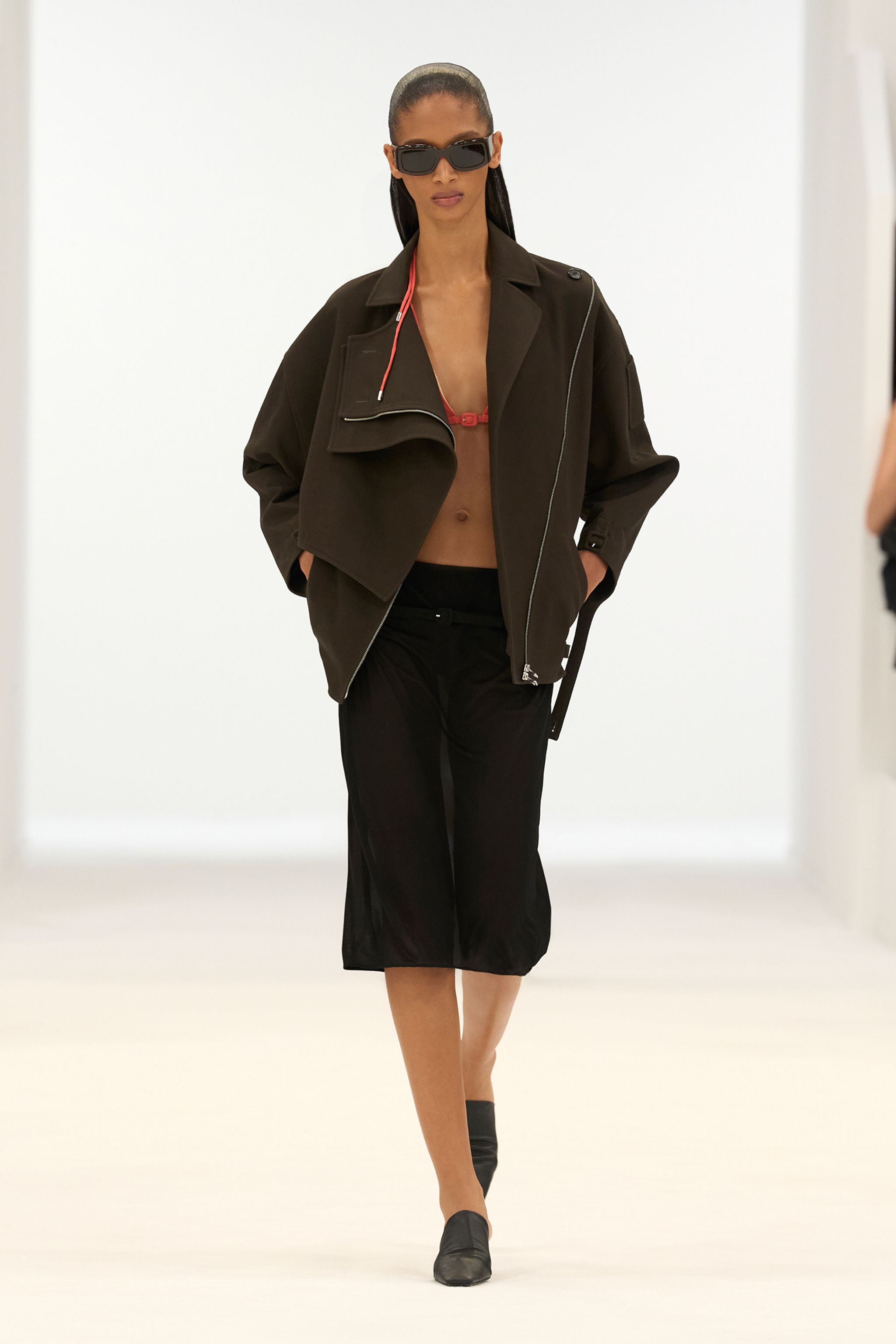 Elegant model wearing Courrèges fashion, black jacket, cropped top, and accessories on runway.