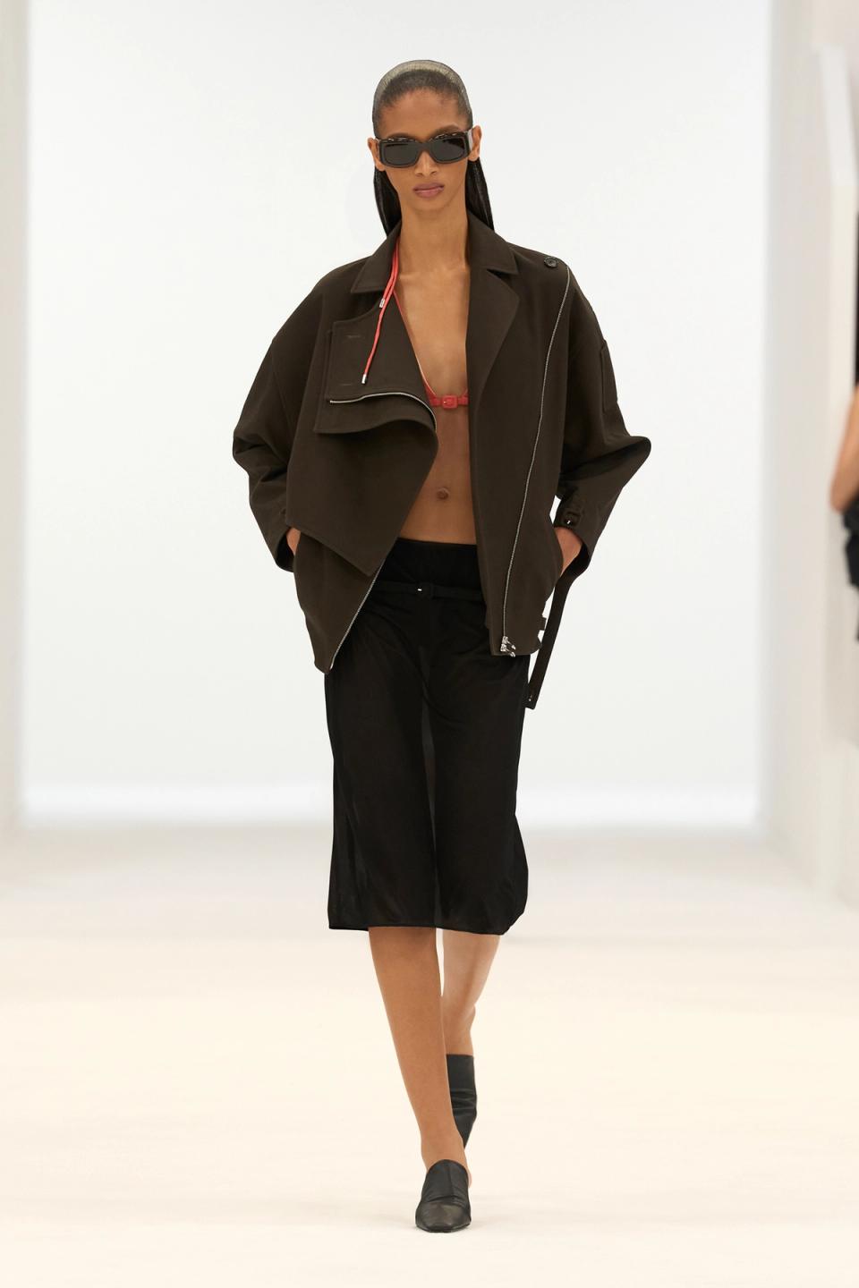 Elegant model wearing Courrèges fashion, black jacket, cropped top, and accessories on runway.