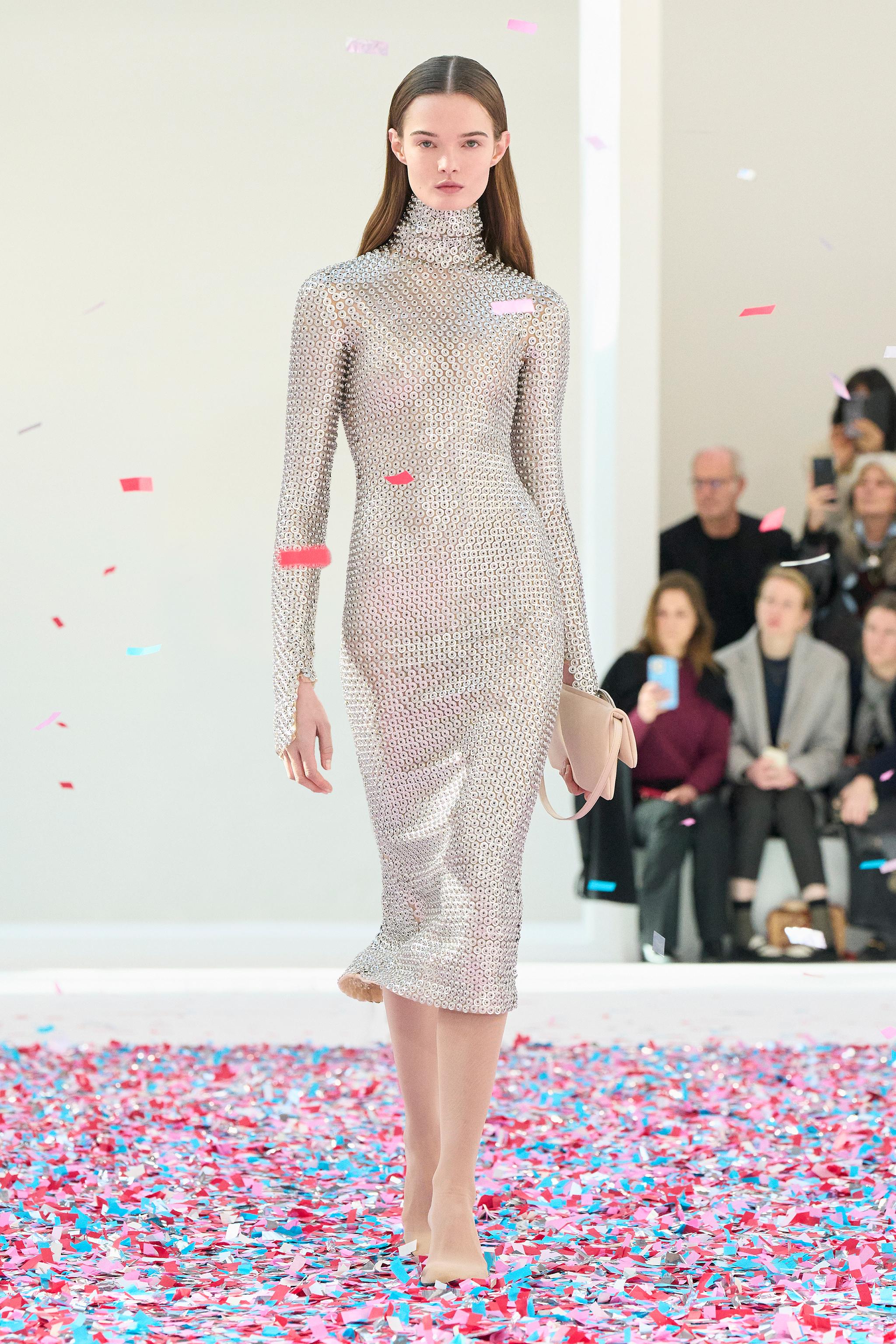 Elegant fashion runway model wearing Courrèges metallic dress on a colorful confetti stage.