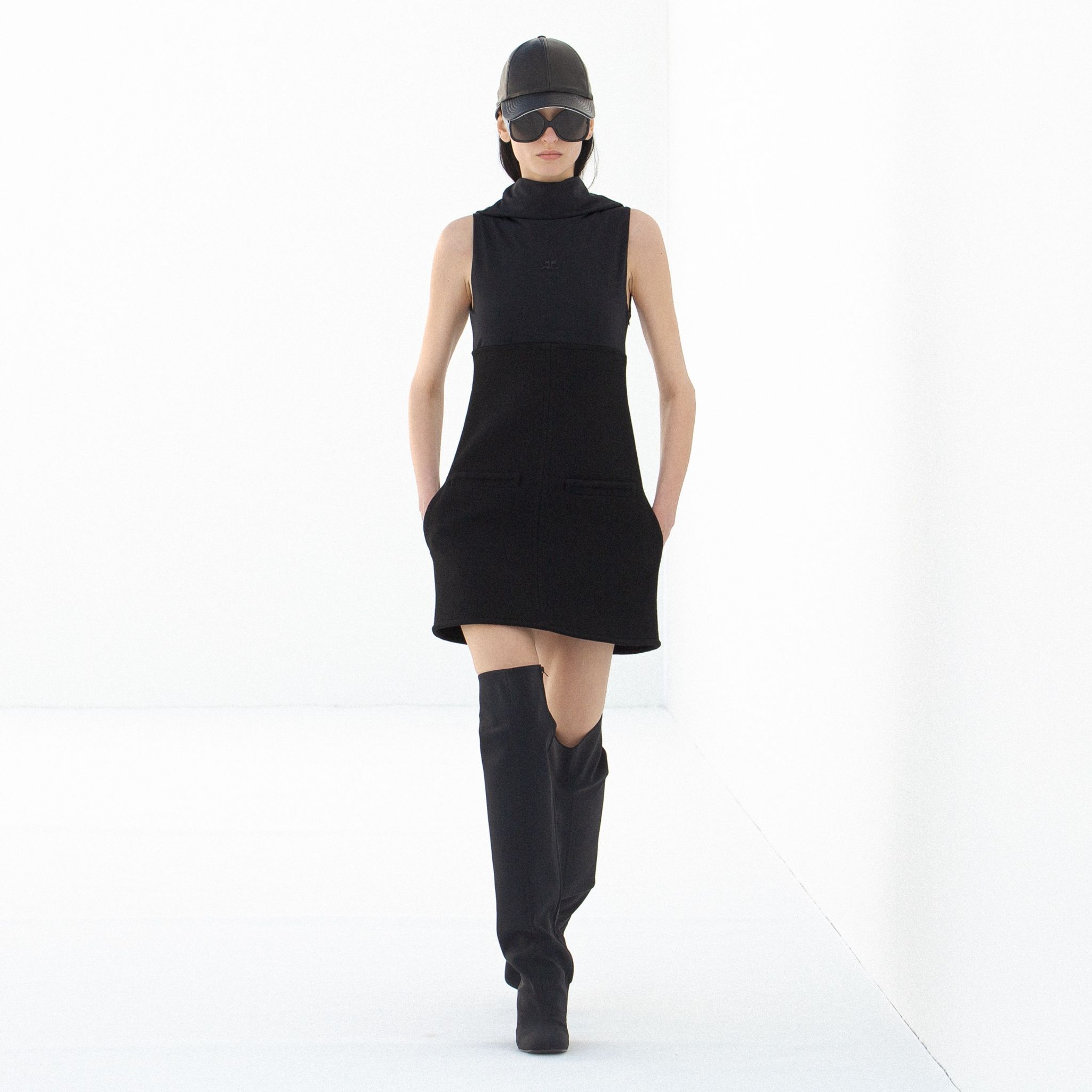 Elegant black sleeveless dress with thigh-high boots, styled for Courrèges fashion.