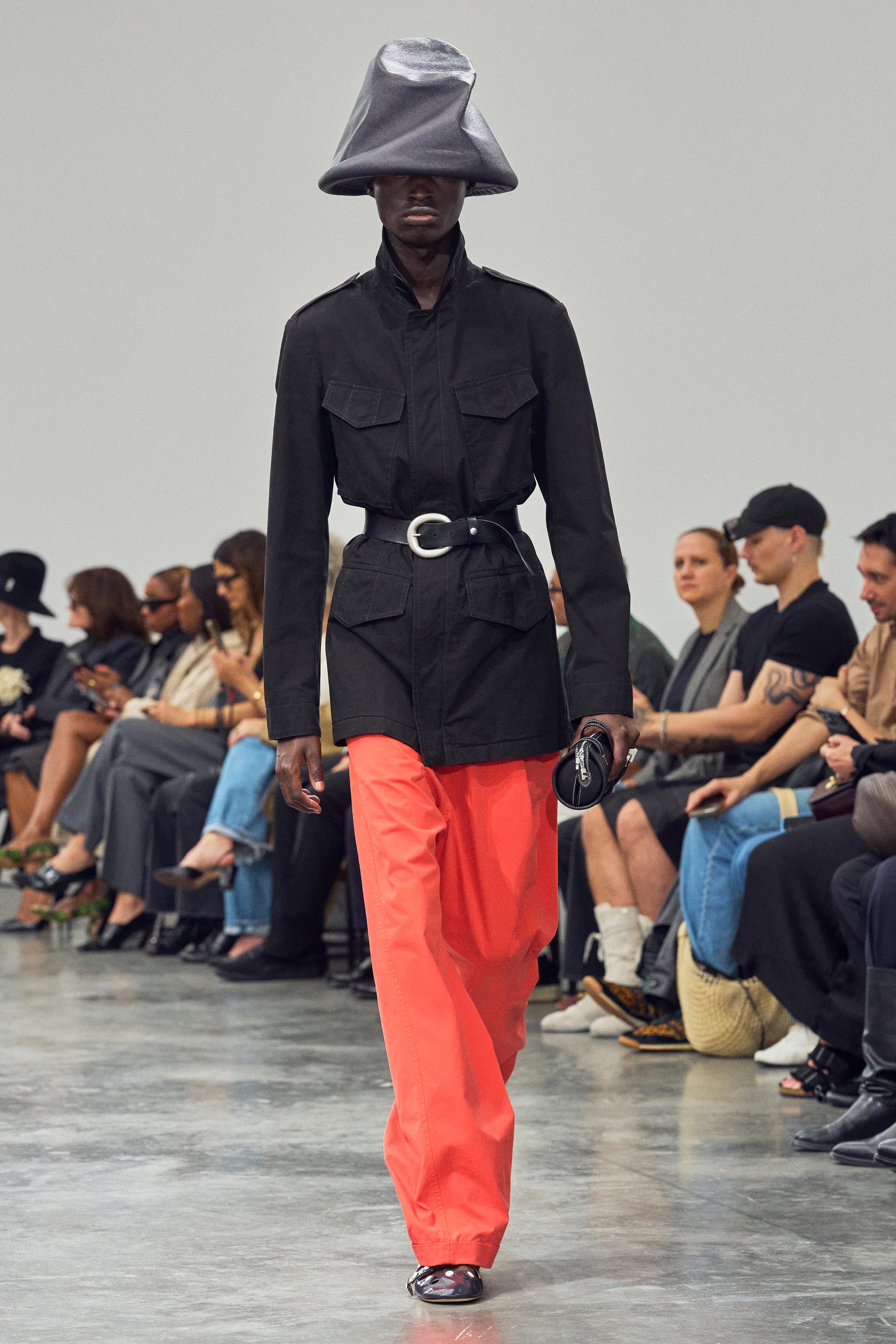 Elegant black jacket with silver buckle and vibrant orange pants by Courrèges on runway.