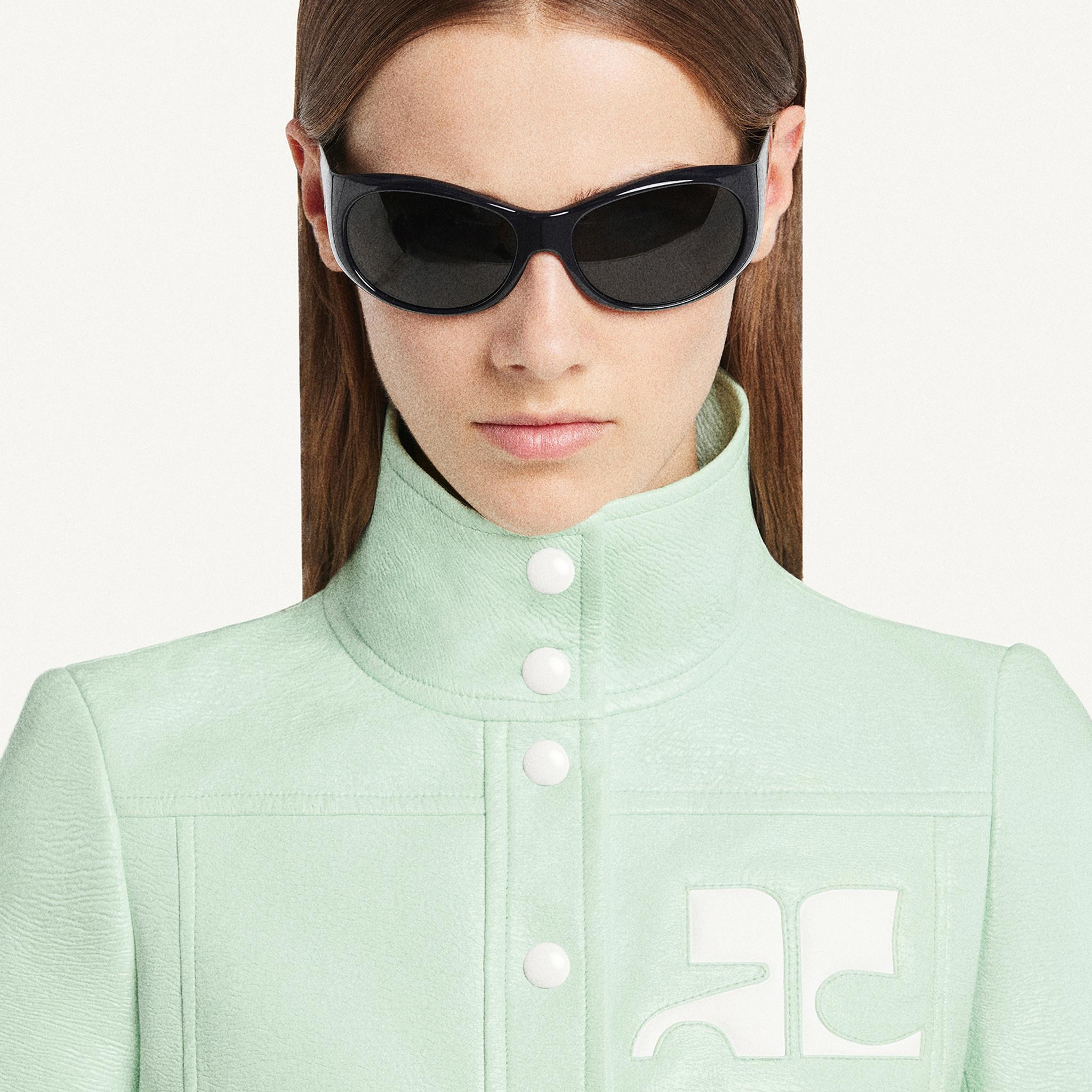 Elegant woman wearing black sunglasses and a mint green high-collar jacket, Courrèges fashion.