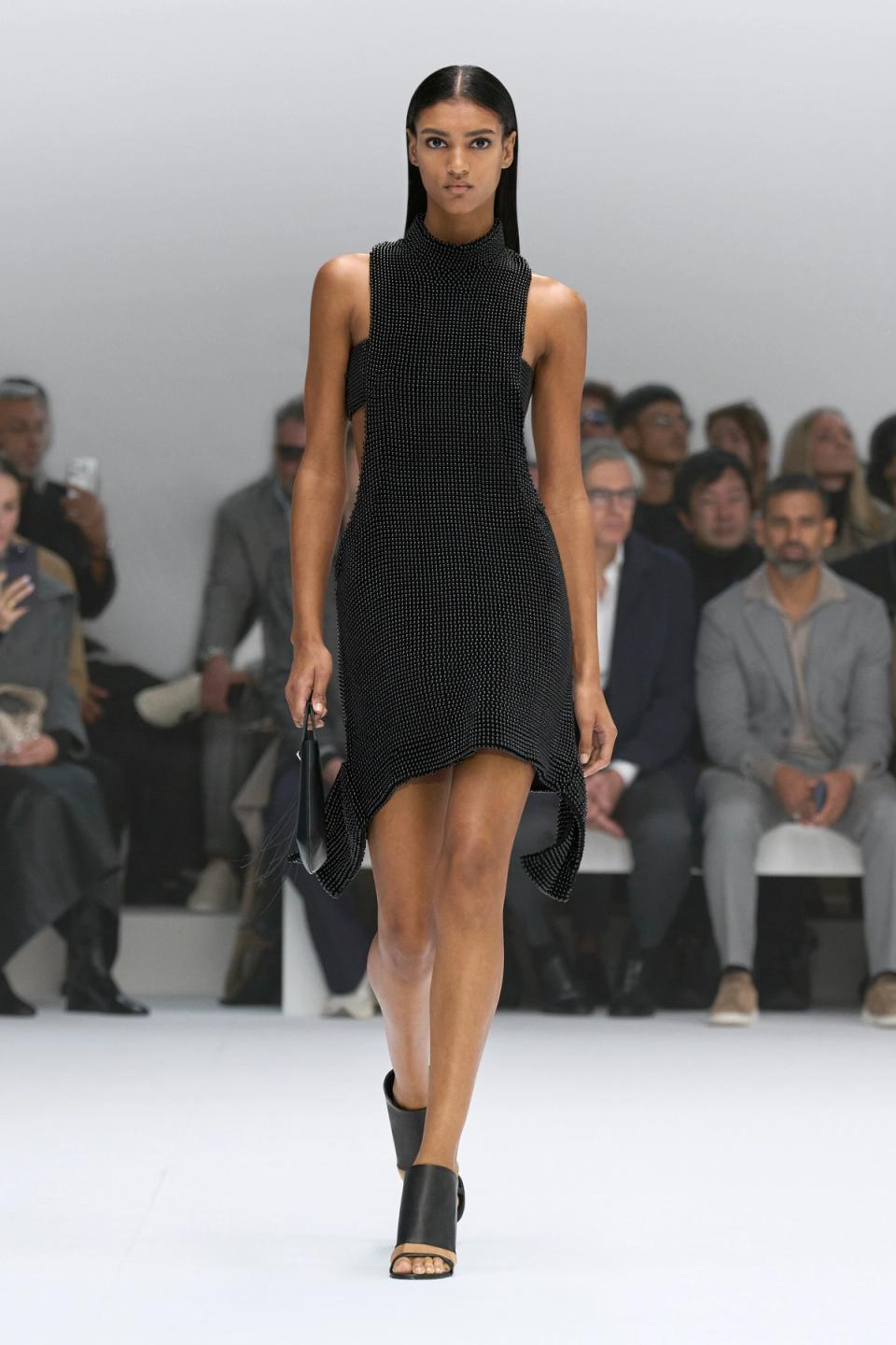 Elegant black dress showcased at Courrèges fashion show on a runway with audience.