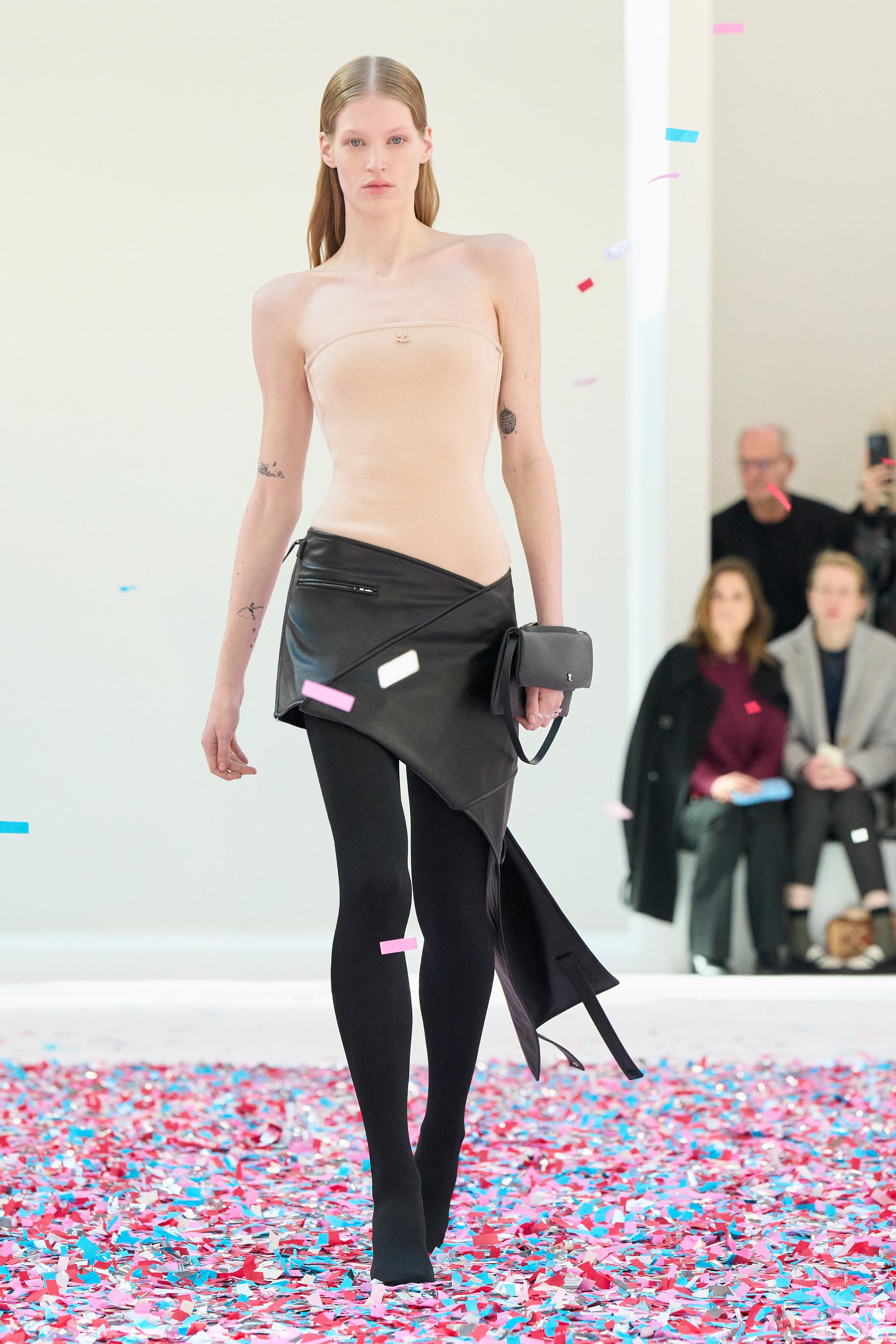 Elegant fashion model walking on confetti, showcasing Courrèges clothing at a fashion show.