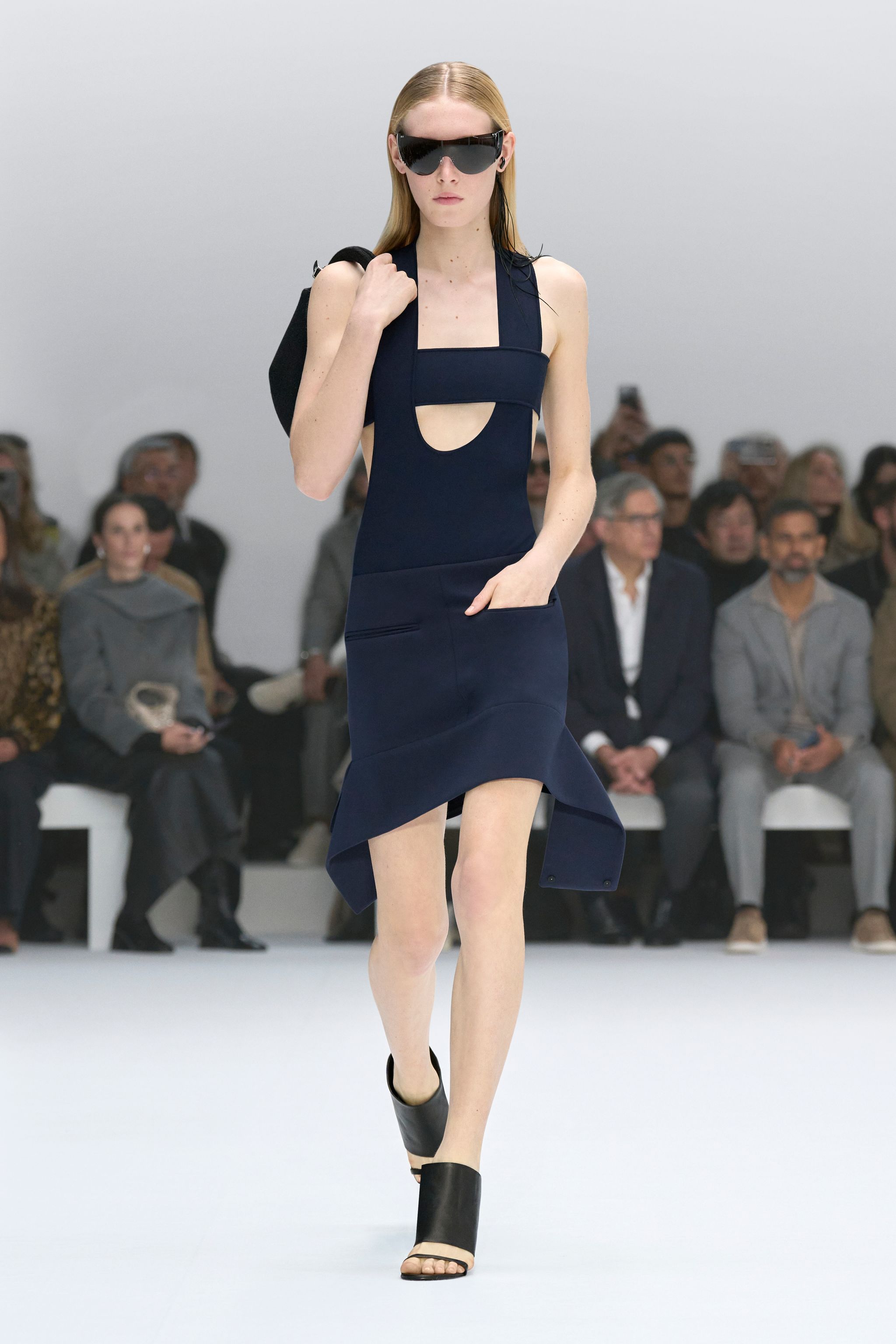 Elegant model wearing a navy blue Courrèges dress with cutouts at a runway show.