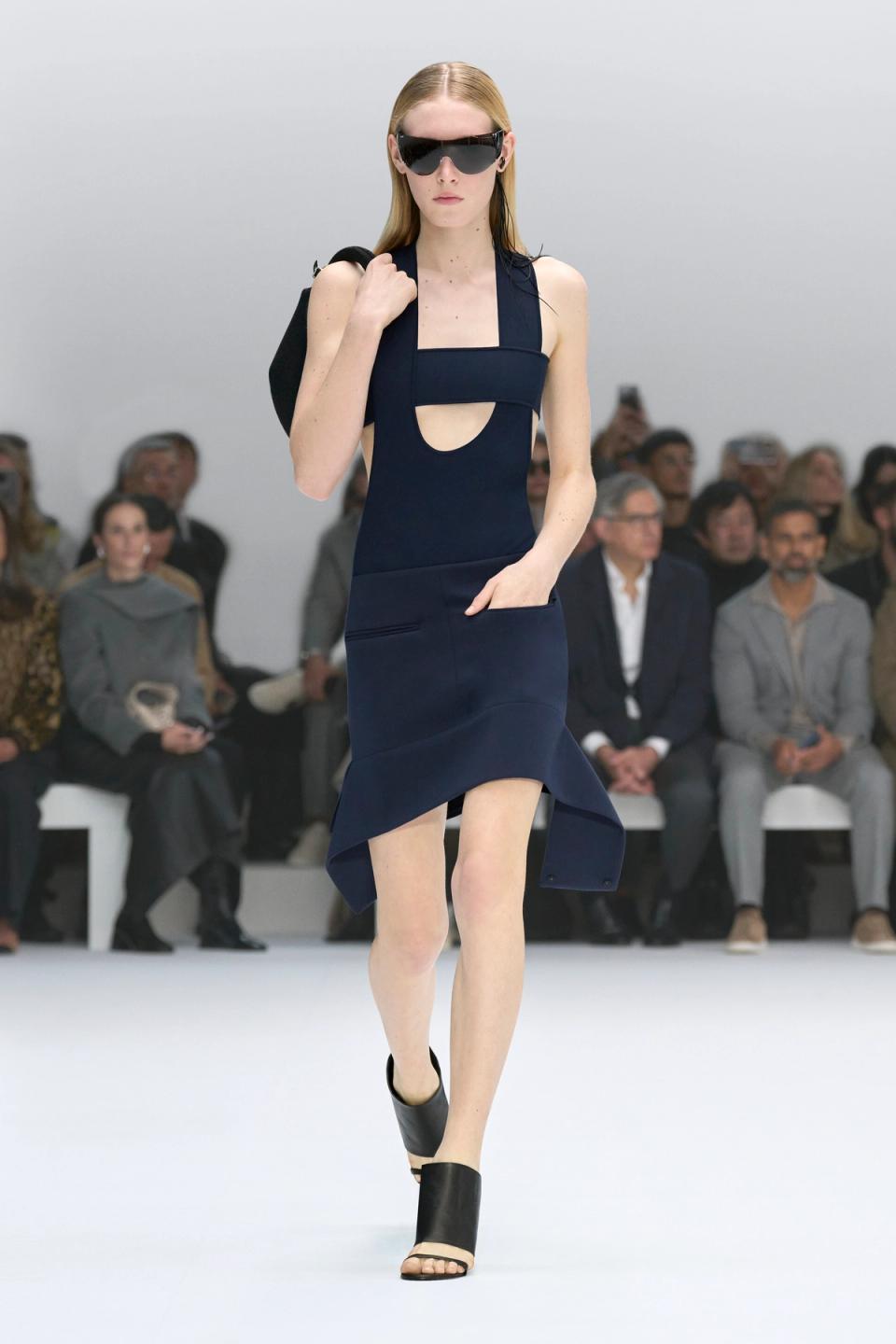 Elegant model wearing a navy blue Courrèges dress with cutouts at a runway show.