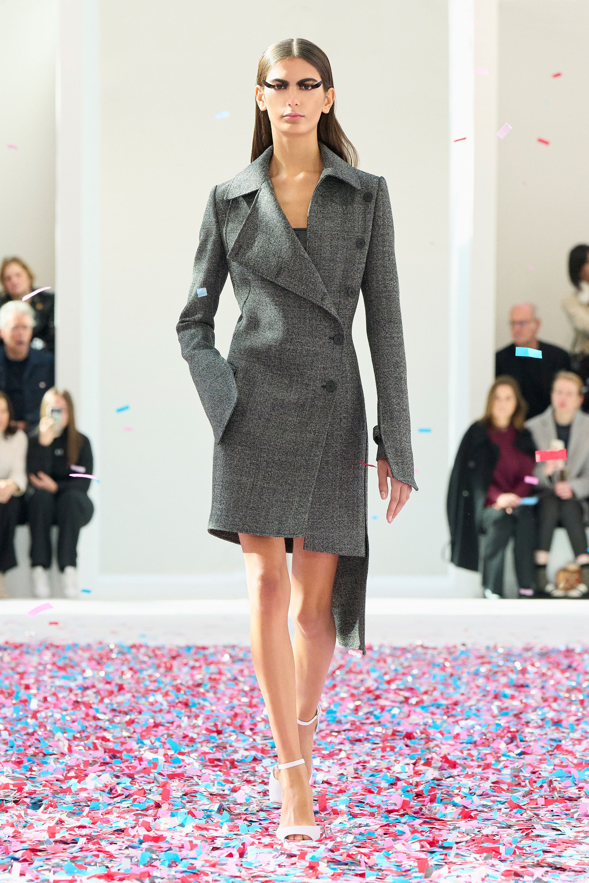 Elegant model wearing a black Courrèges coat on runway with colorful confetti, for ecommerce.