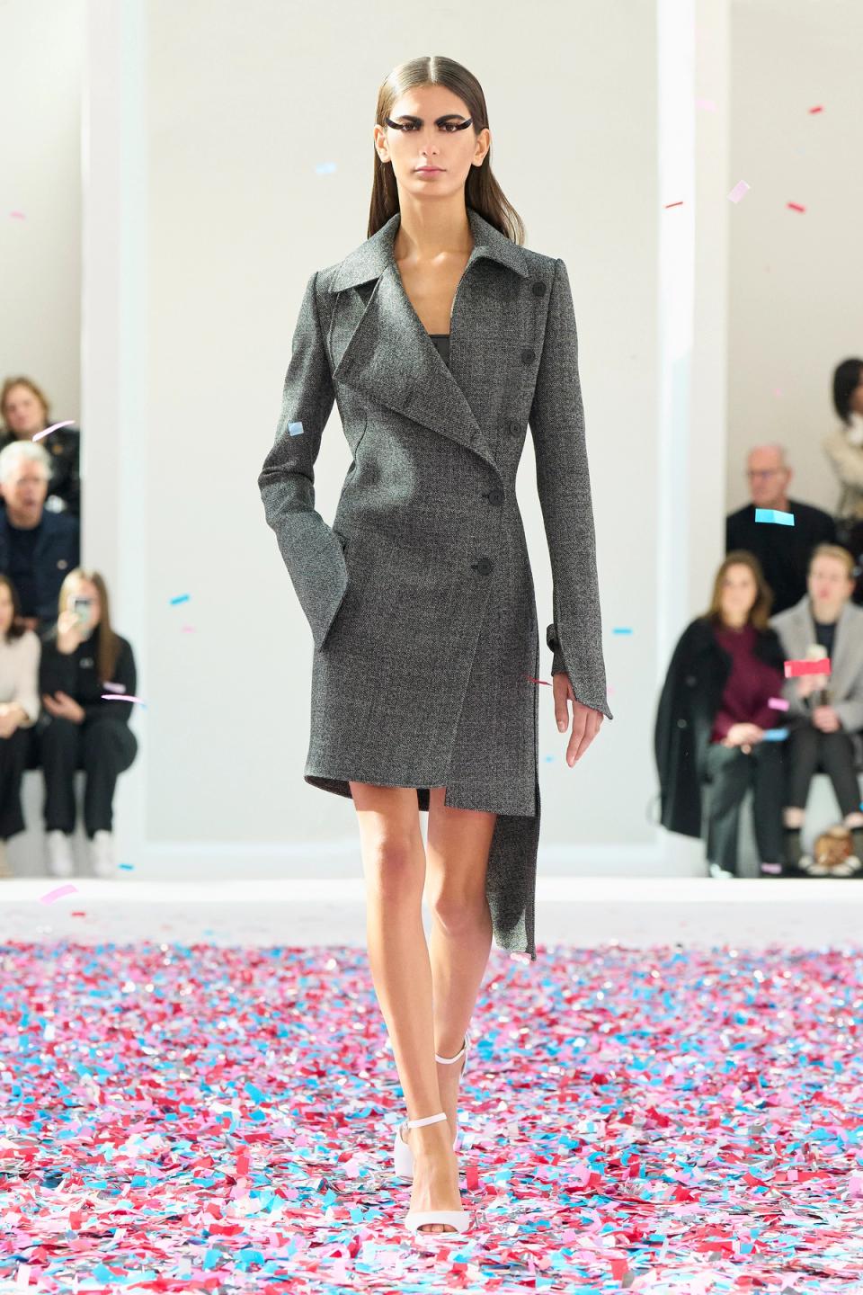 Elegant model wearing a black Courrèges coat on runway with colorful confetti, for ecommerce.