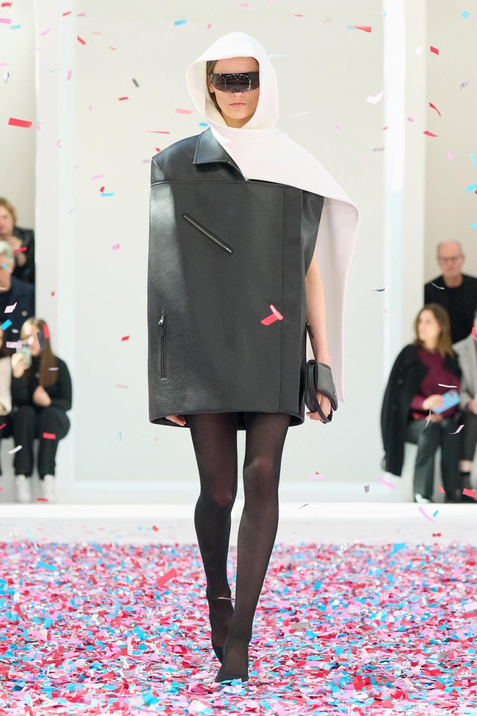 Fashion model in avant-garde outfit at Courrèges collection unveiling, surrounded by confetti.