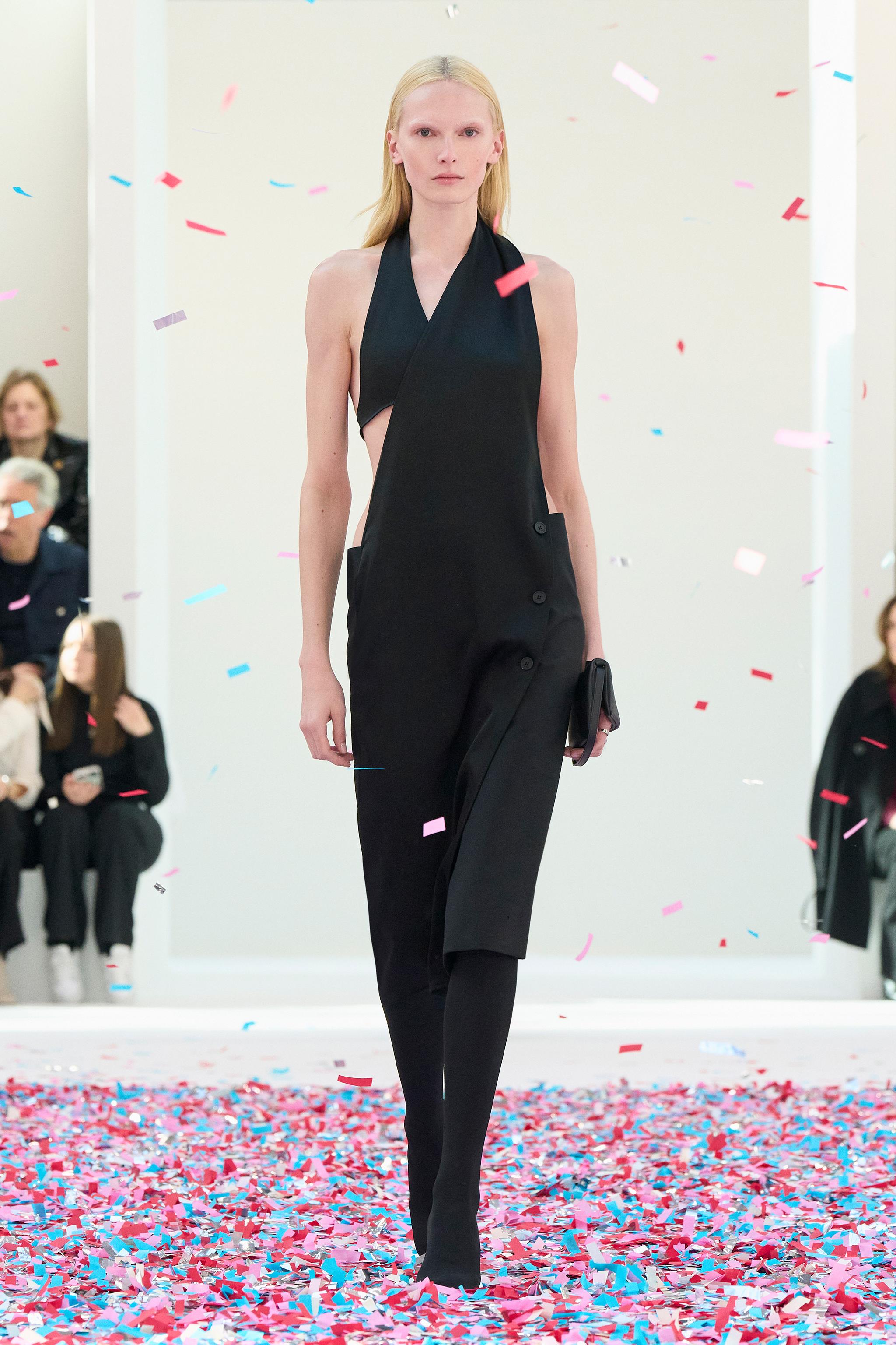 Elegant black satin asymmetric dress by Courrèges showcased on the runway with confetti.