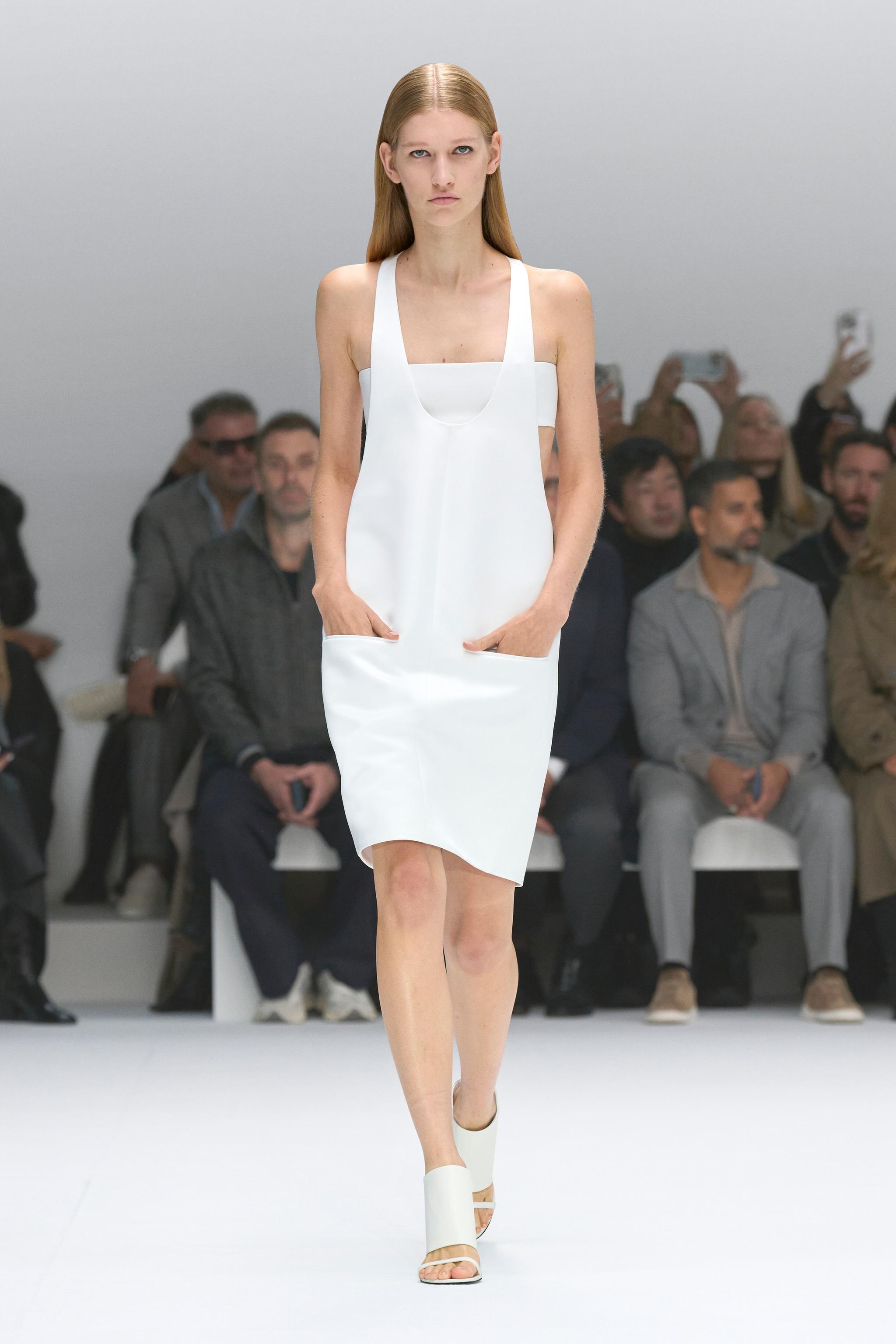Elegant white dress by Courrèges showcased on a runway, capturing modern minimalist fashion.