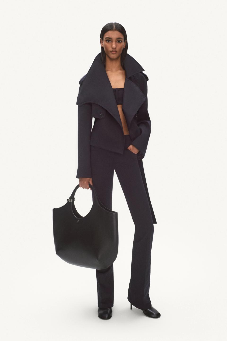 Elegant youthful woman in navy trench coat with black handbag for Courrèges fashion ecommerce