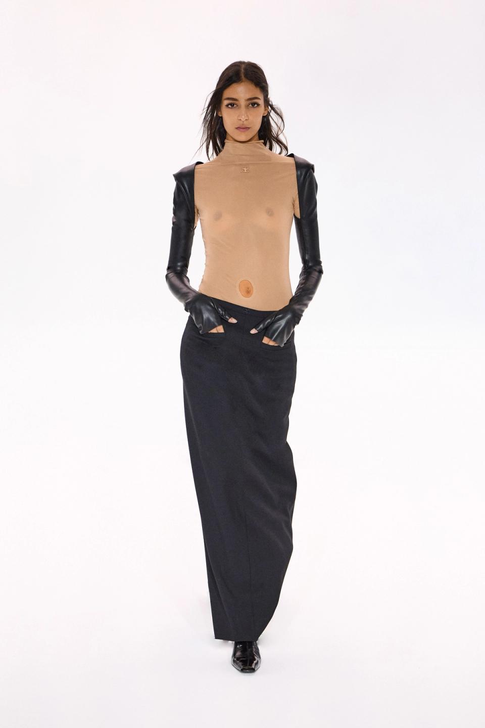 Elegant female model in beige mesh top and black leather-sleeved dress on white background for Courrèges.