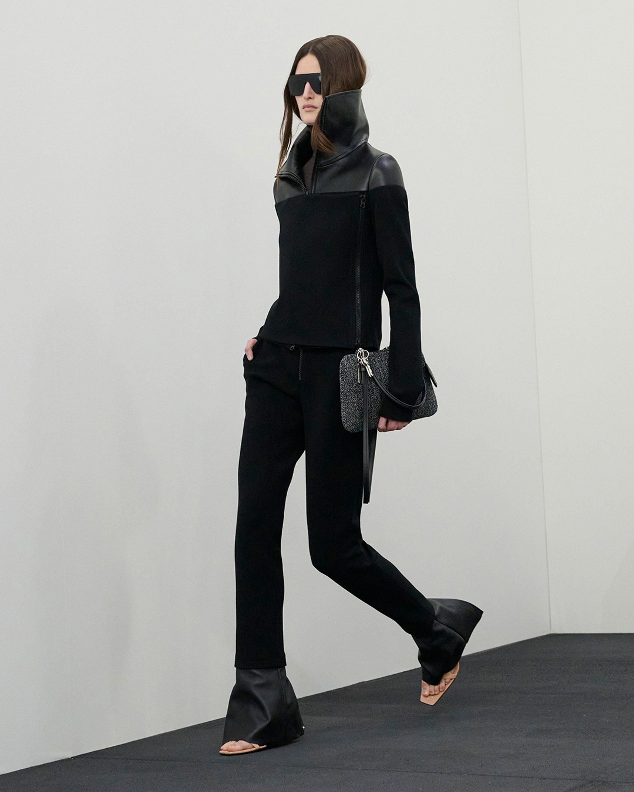 Tenue élégante noire avec détails en cuir et lunettes de soleil oversize, collection de Courrèges.