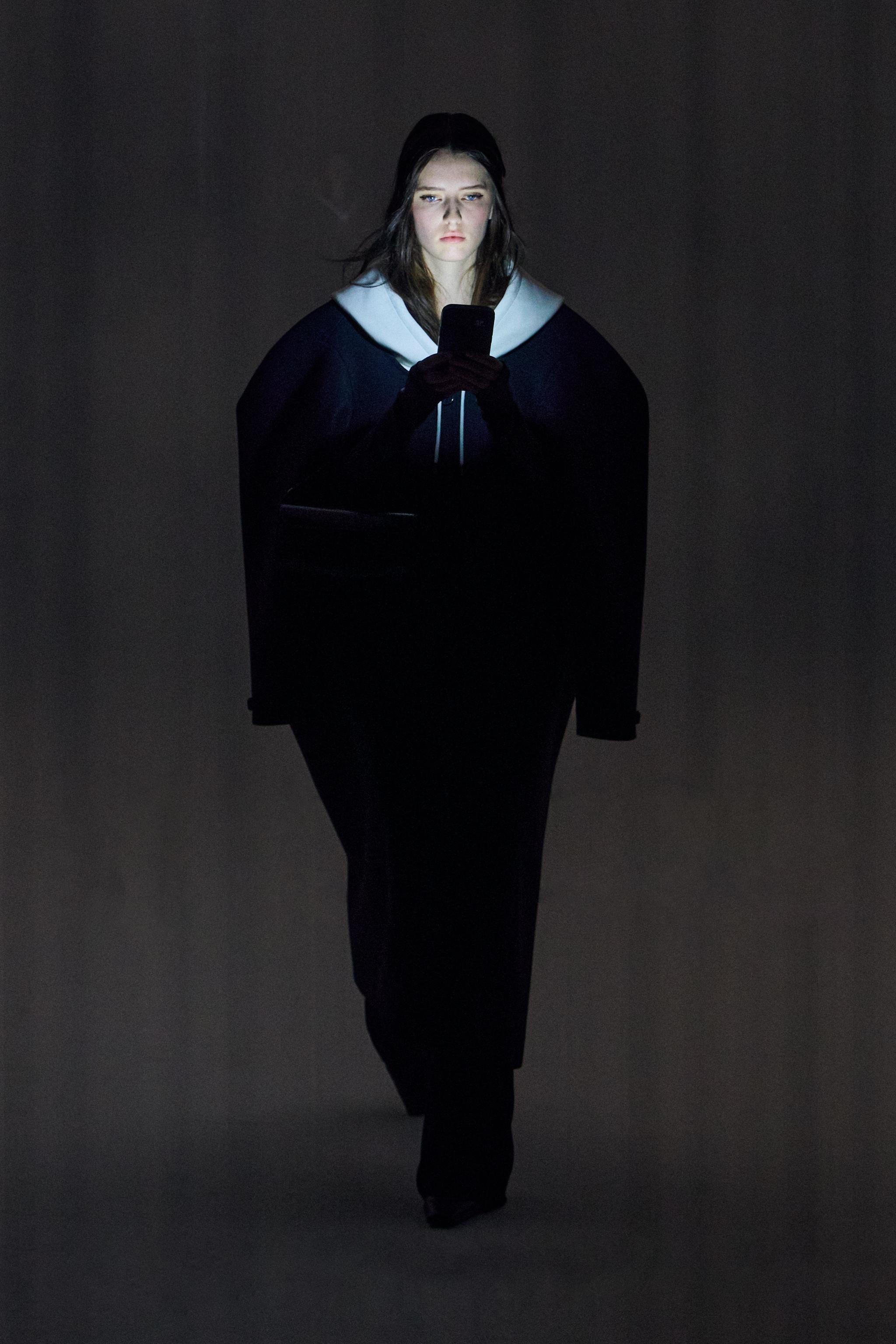 Elegant woman in dark fashion outfit using a smartphone against a modern background, Courrèges.