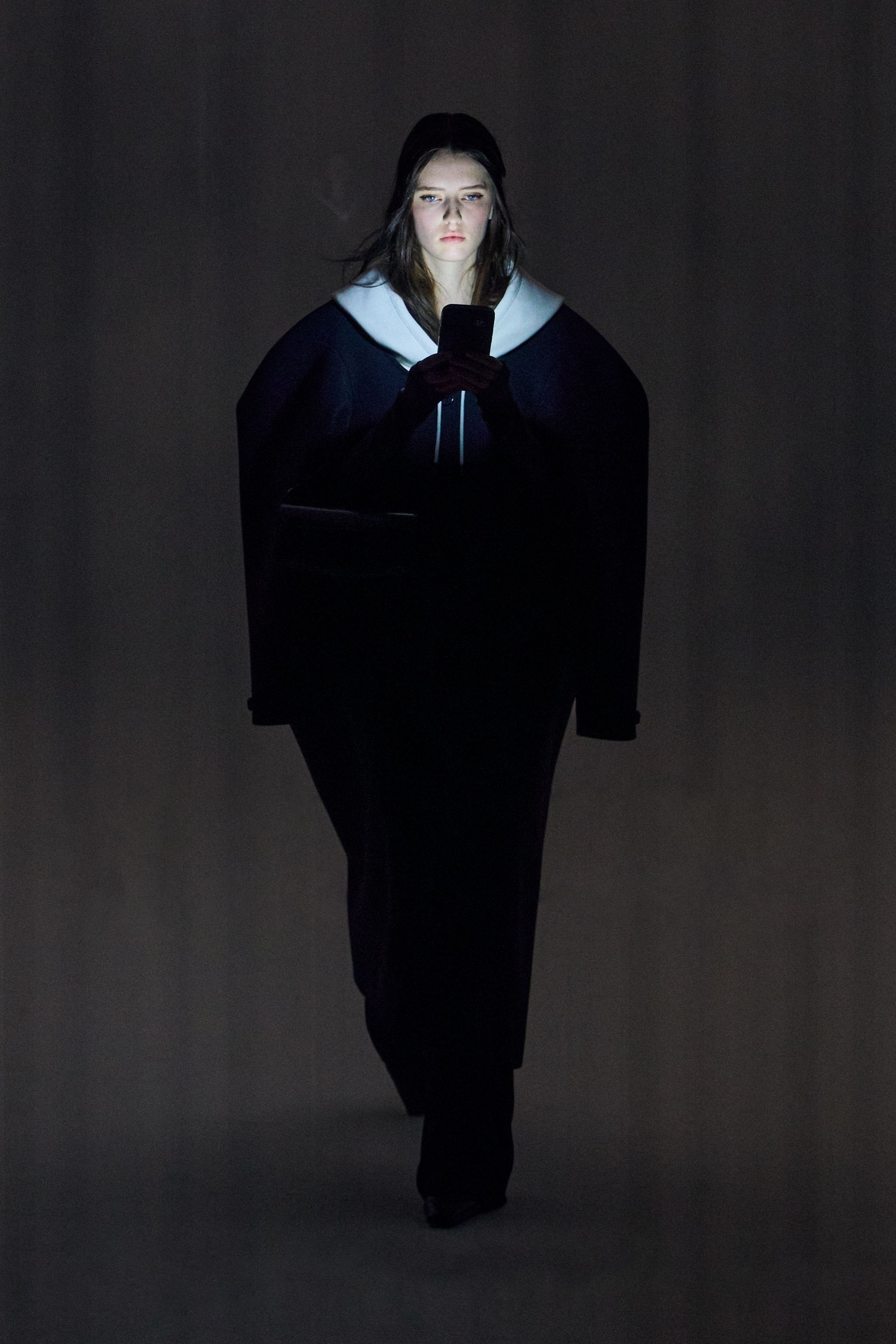 Elegant woman browsing on her smartphone in a dark setting, associated with Courrèges fashion.