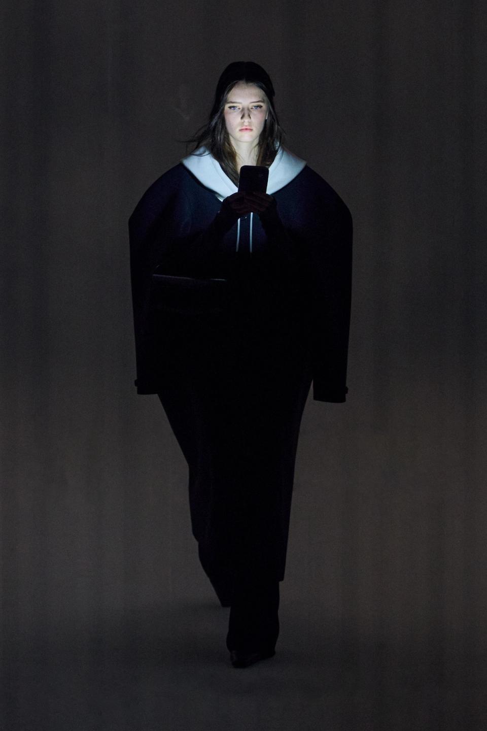 Elegant woman browsing on her smartphone in a dark setting, associated with Courrèges fashion.