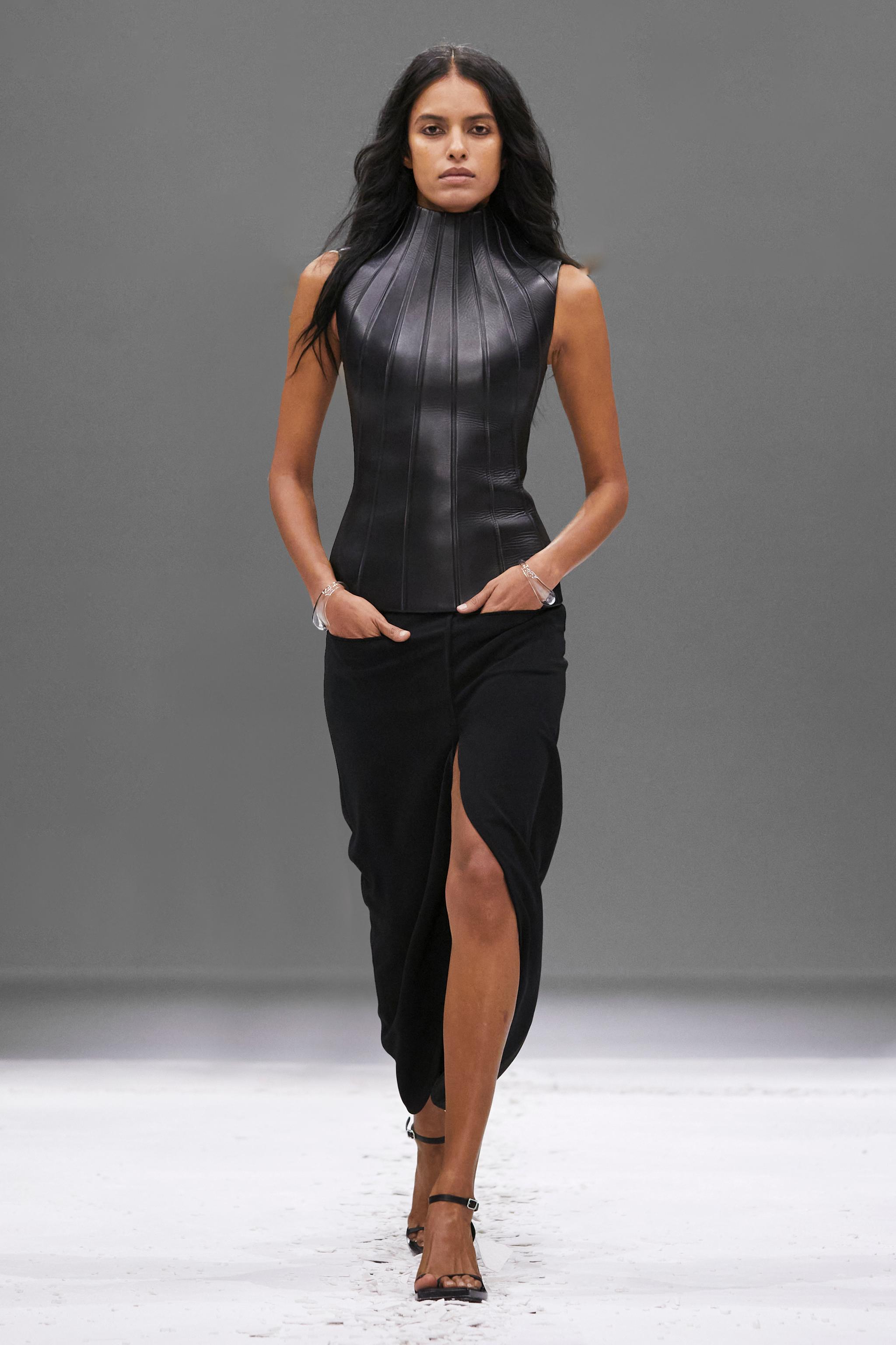 Elegant female model in a sleek black leather top and flowing skirt on runway, Courrèges fashion.