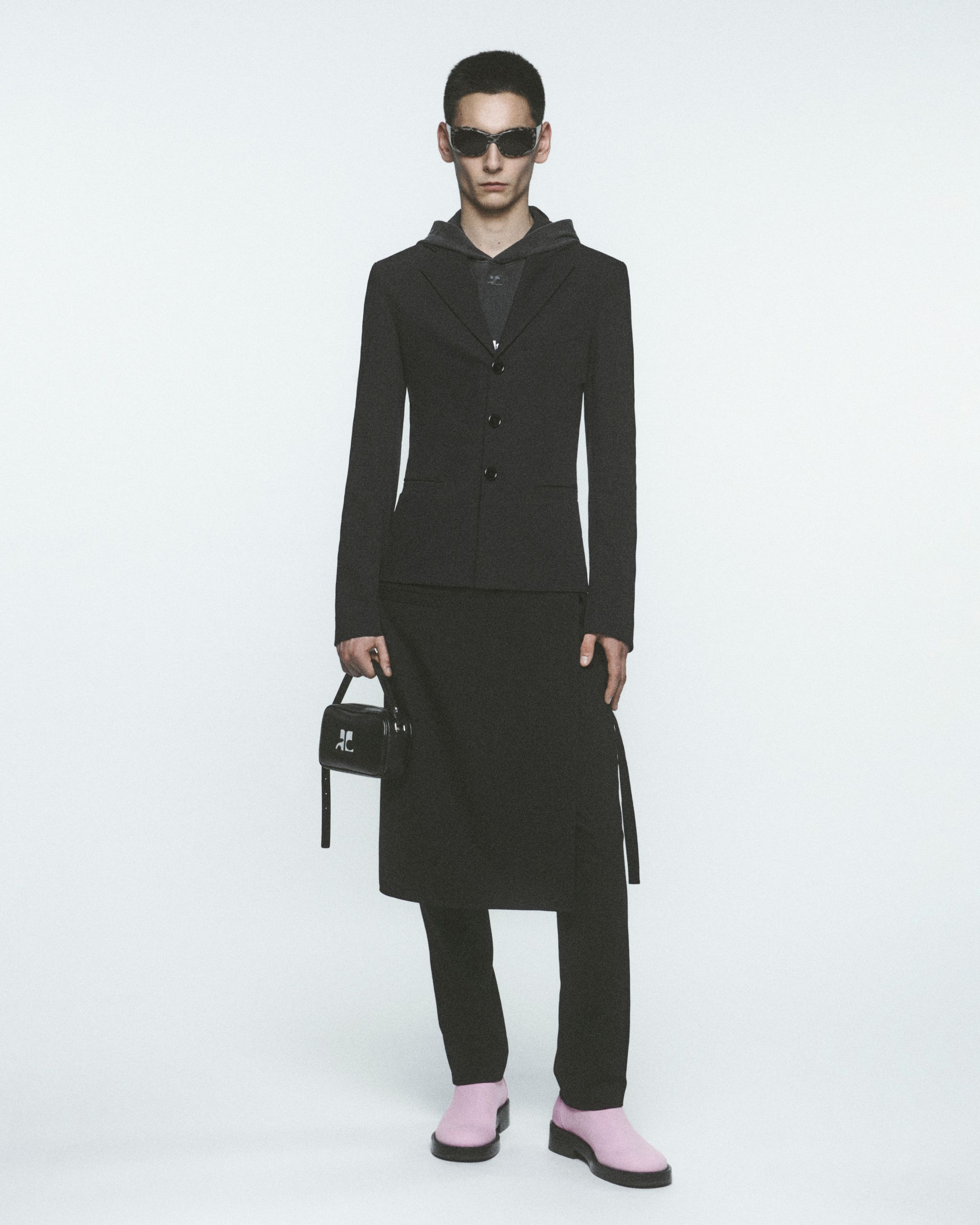 Modèle élégant portant une tenue Courrèges noire et des bottes roses dans un contexte de site web.