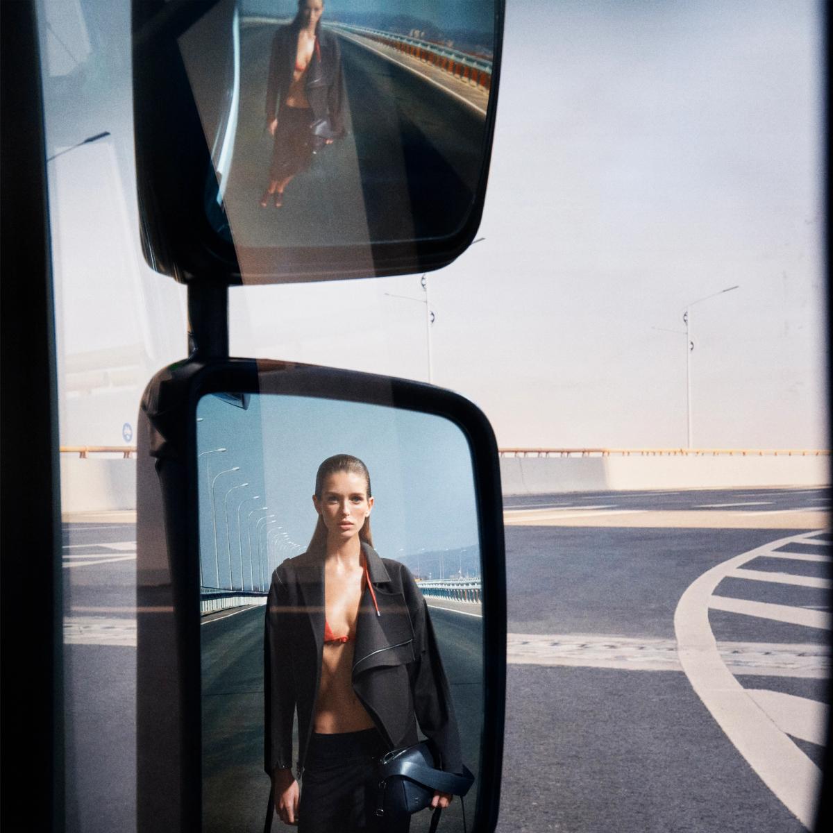 Elegant fashion model reflected in side mirror, showcasing Courrèges style on urban road.