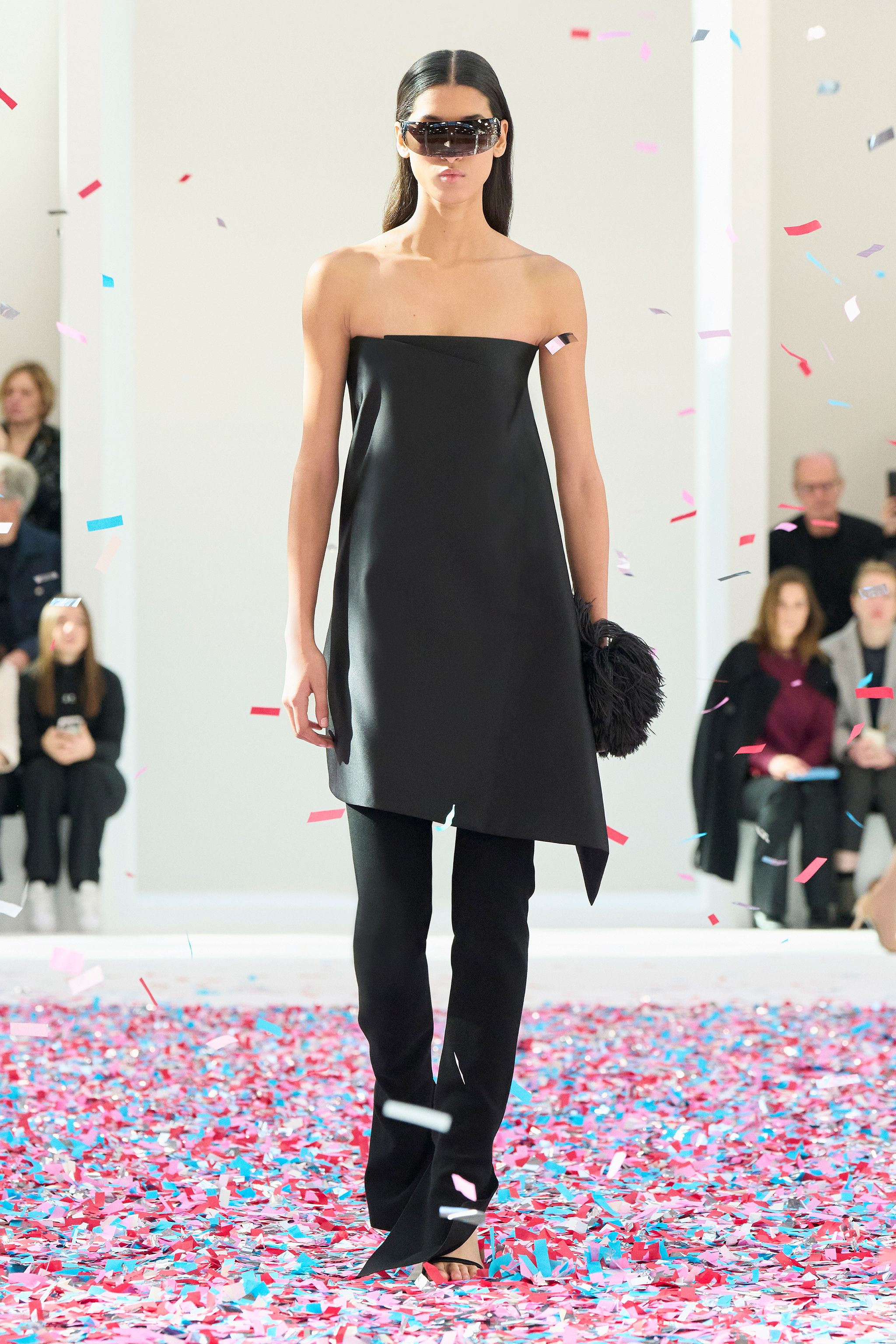 Elegant black strapless dress by Courrèges showcased on runway with colorful confetti.