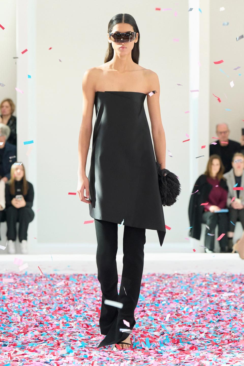 Elegant black strapless dress by Courrèges showcased on runway with colorful confetti.