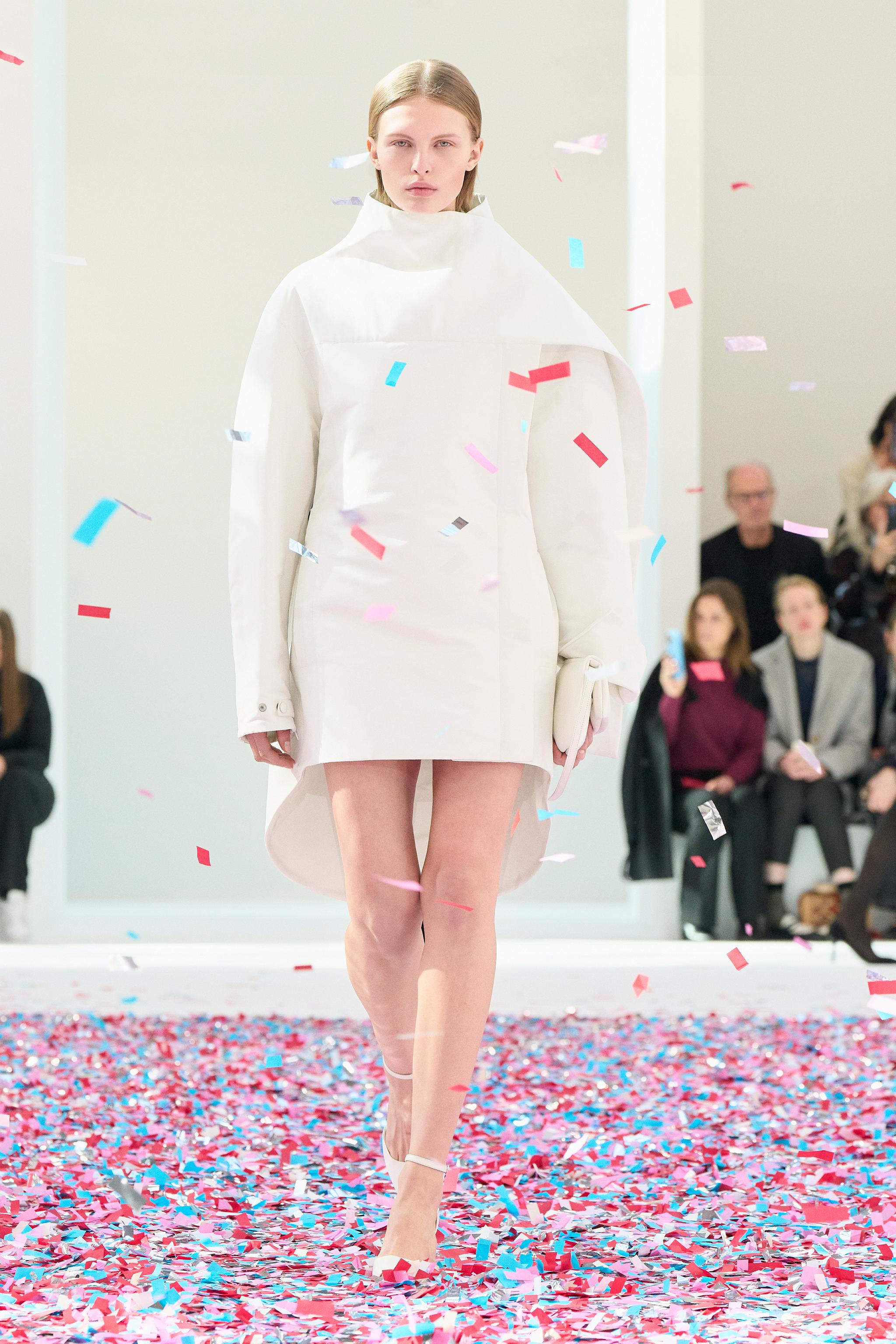 Elegant white coat and fashionable heels at Courrèges fashion show with colorful confetti.