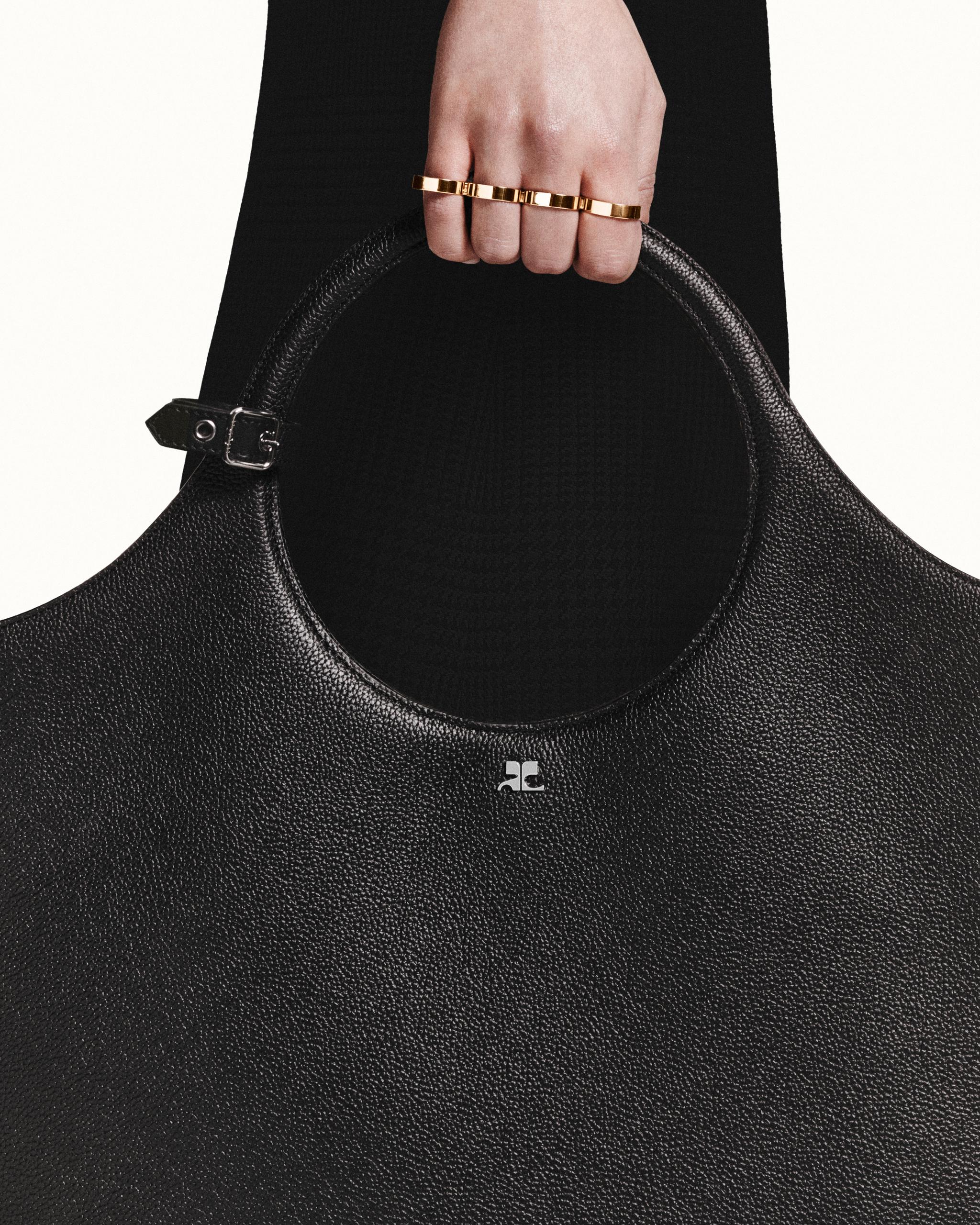 Elegant black textured leather handbag with curvilinear handle, showcasing Courrèges luxury fashion.
