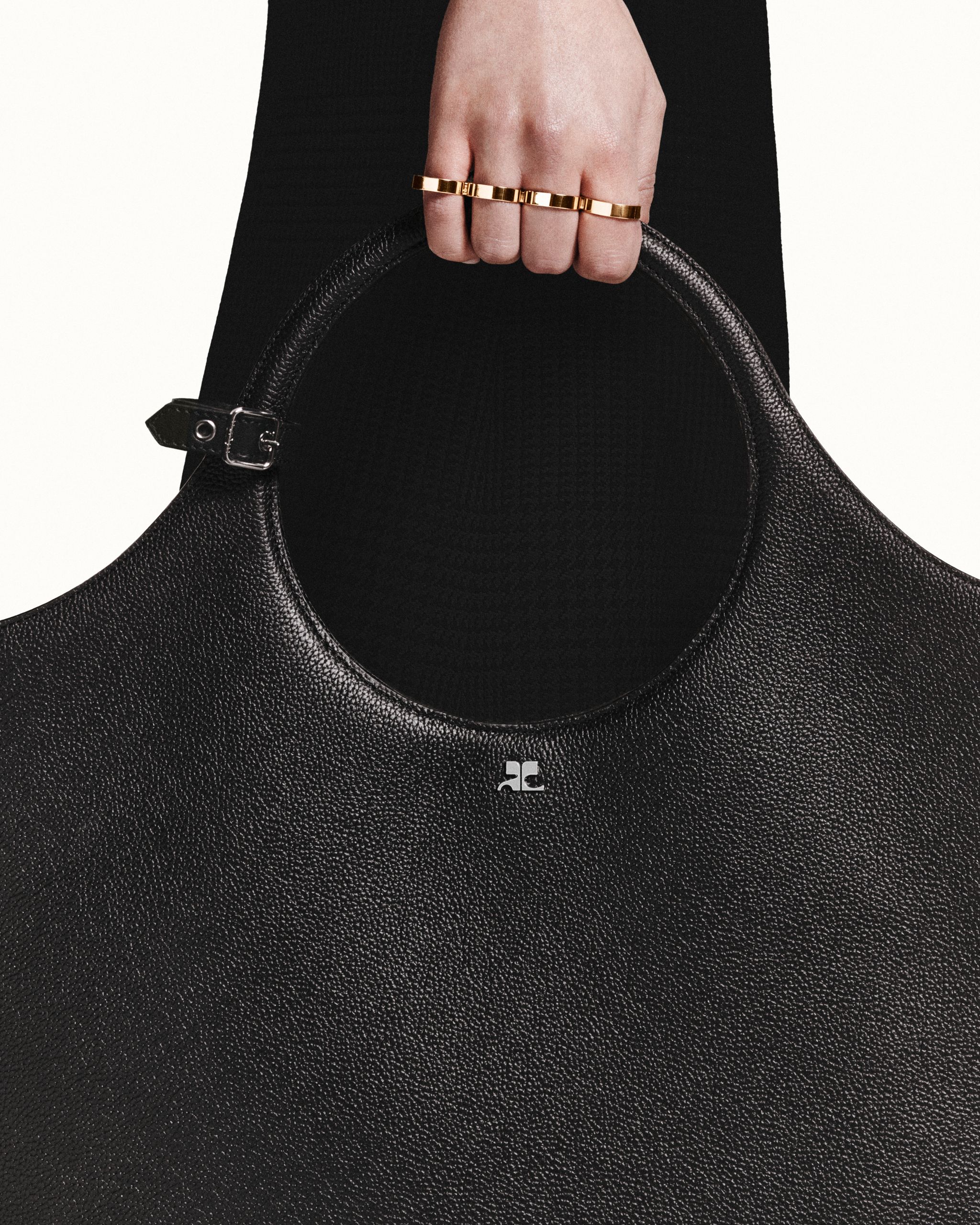 Elegant black textured leather handbag with curvilinear handle, showcasing Courrèges luxury fashion.