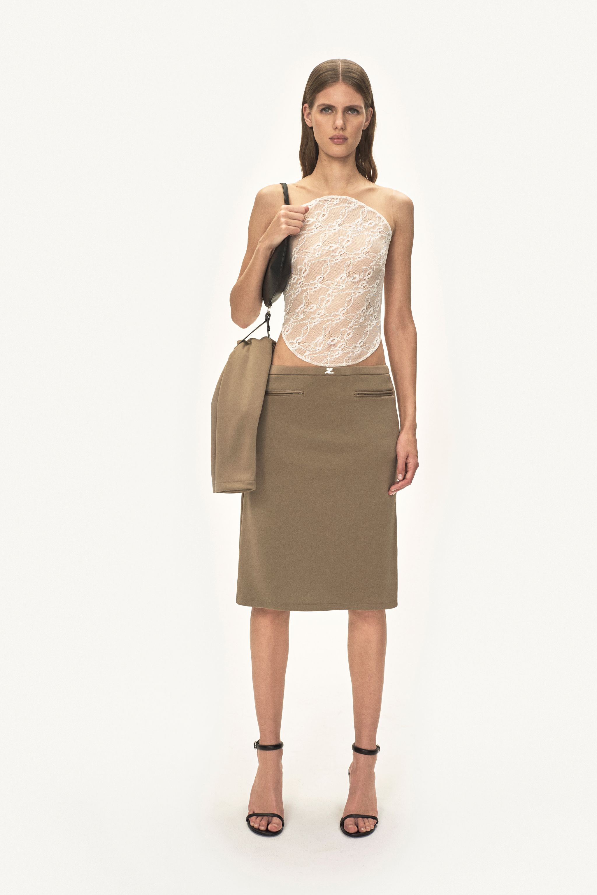 Elegant model in Courrèges fashion, wearing a lace top and beige skirt, carrying a bag, on an ecommerce site.