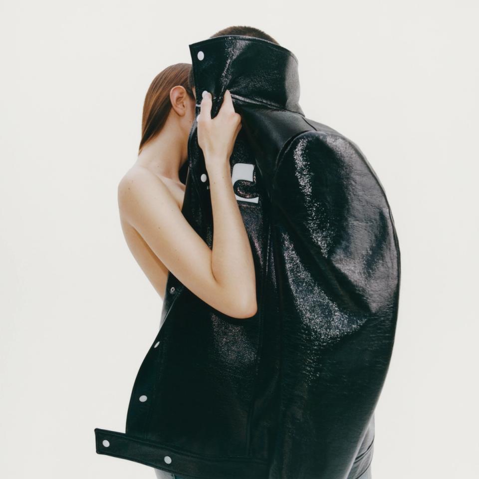 Mannequin partiellement caché par une veste surdimensionnée en cuir verni noir, pose minimaliste.