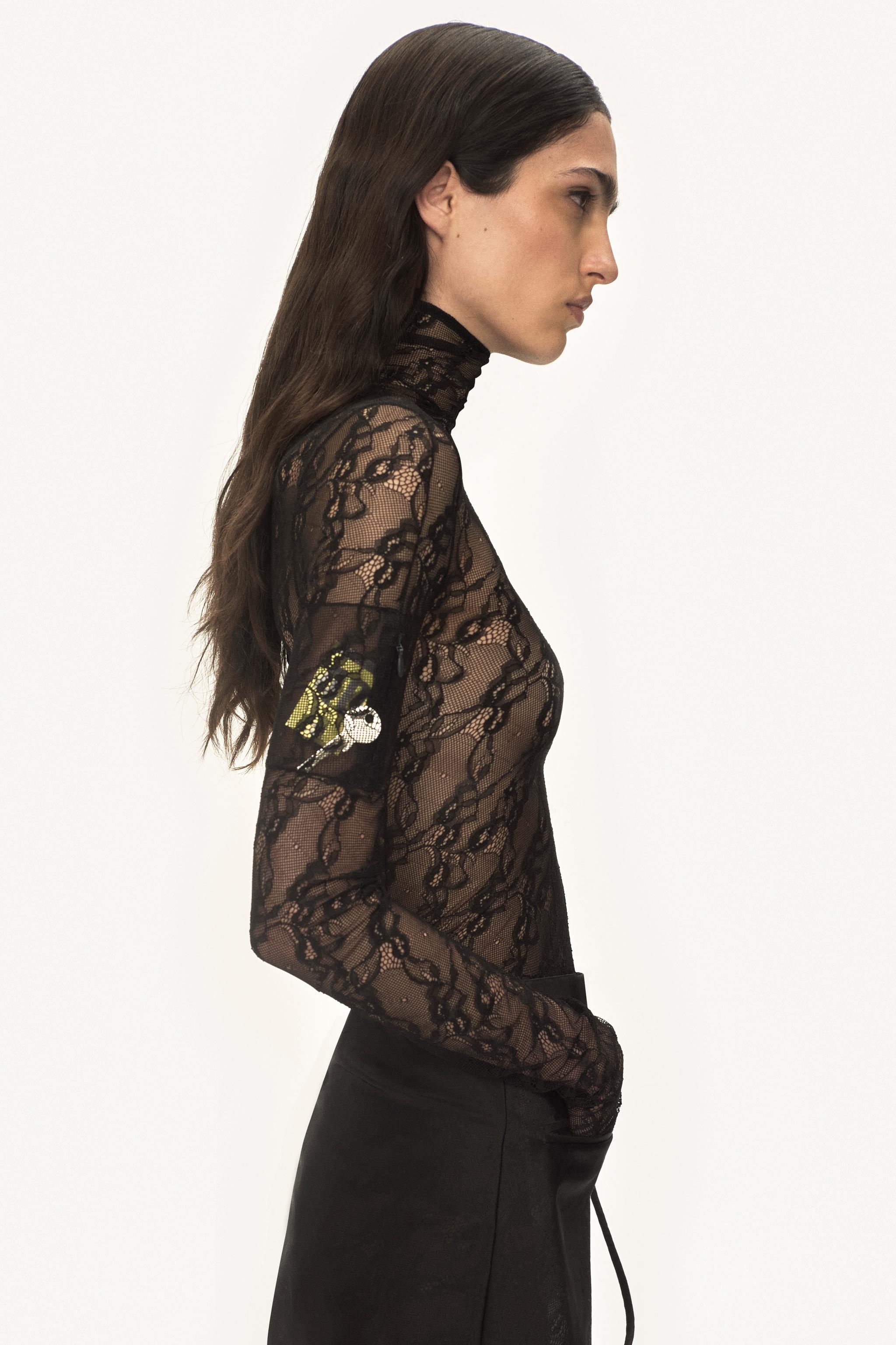 T-shirt noir en dentelle avec col roulé de Courrèges porté par un mannequin de mode.