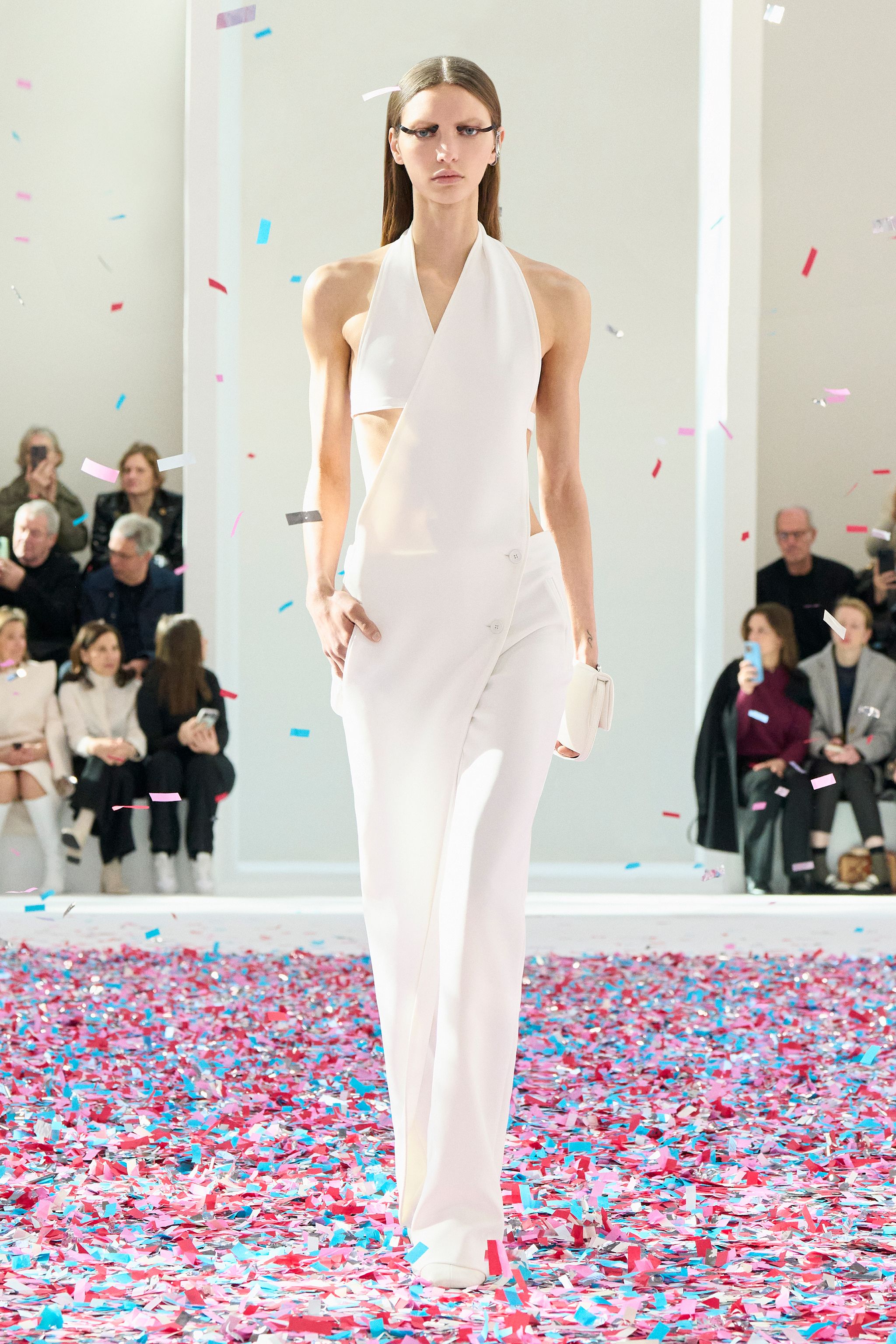 Elegant white modern jumpsuit by Courrèges showcased on a runway with colorful confetti.