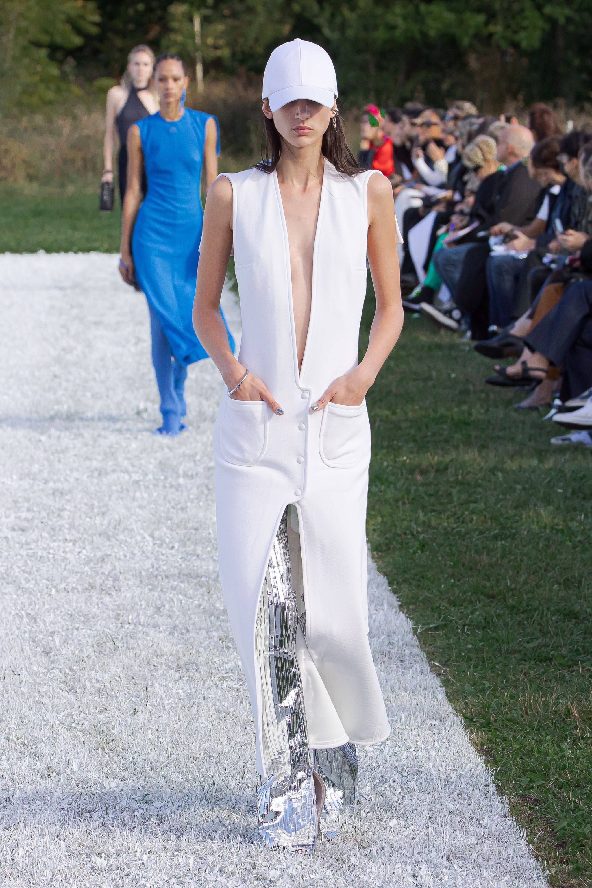 Model walking runway in elegant Courrèges white sleeveless jumpsuit with metallic details.