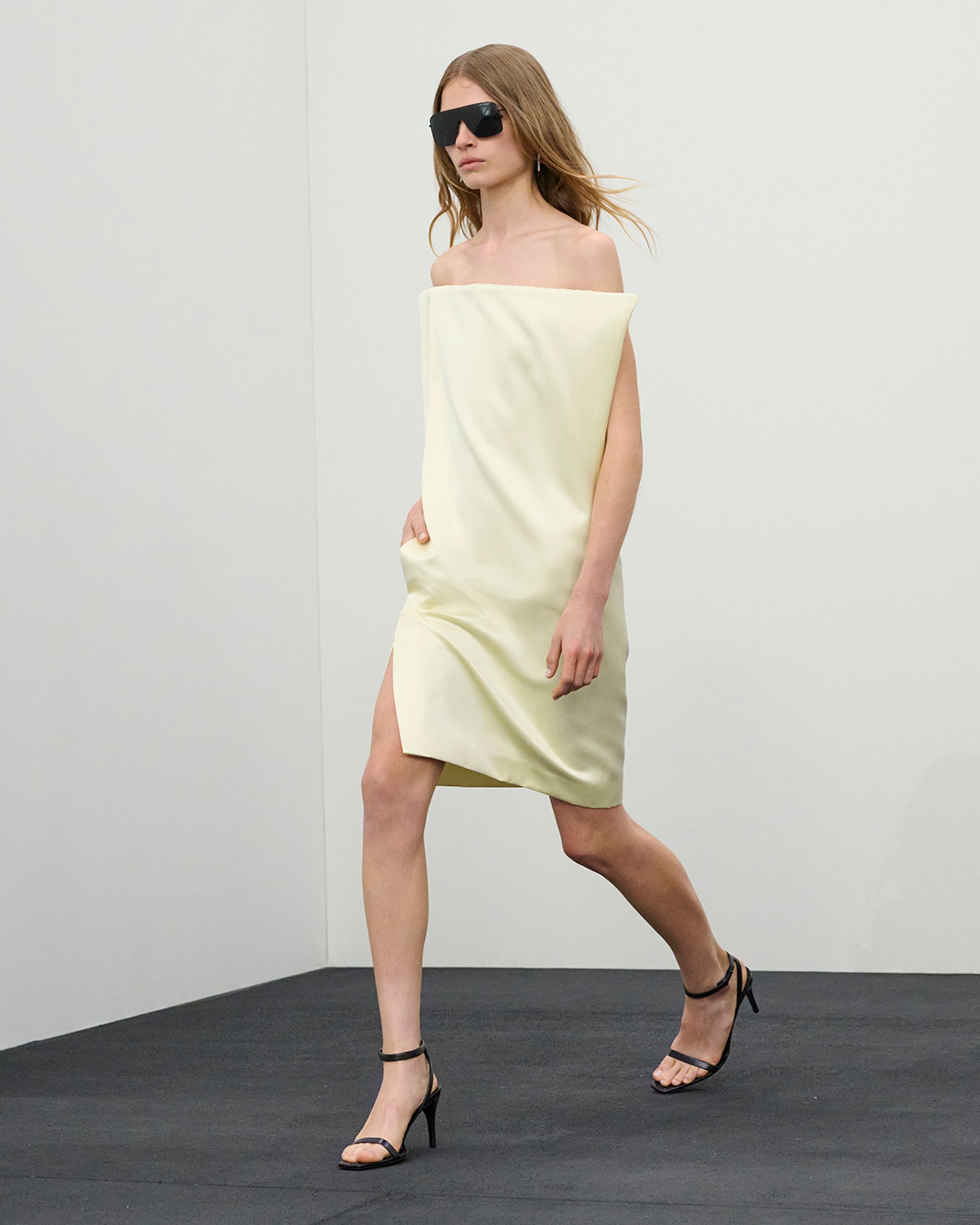 Femme élégante en robe ensoie asymétrique, avec des lunettes de soleil tendance, pour Courrèges.