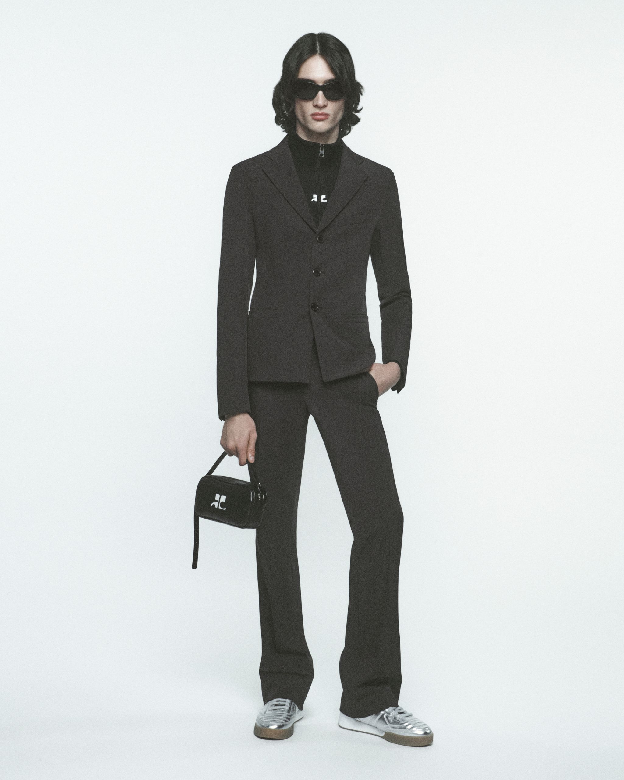 Costume élégant noir de Courrèges avec baskets, lunettes de soleil et sac à main tendance.