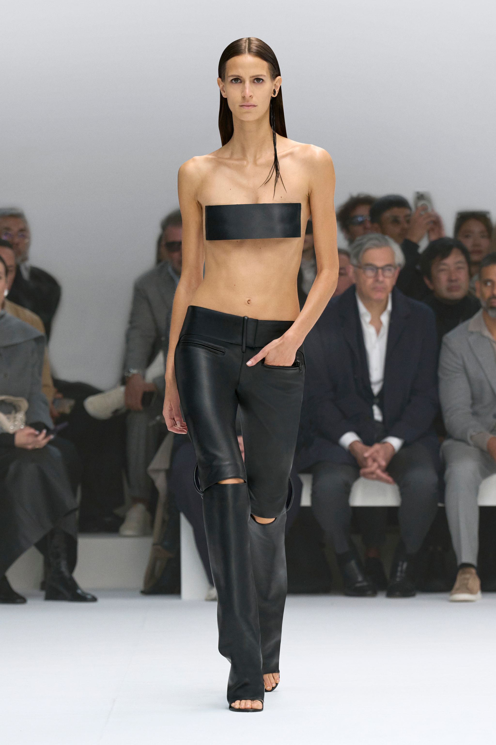 Elegant fashion runway model showcasing Courrèges black leather pants and minimal top.