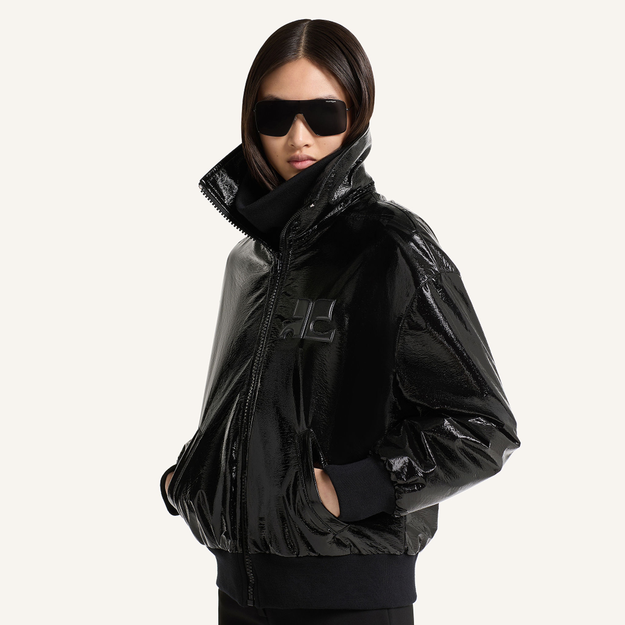 Veste noire brillante Courrèges élégante avec col droit et lunettes de soleil, portée par un mannequin.