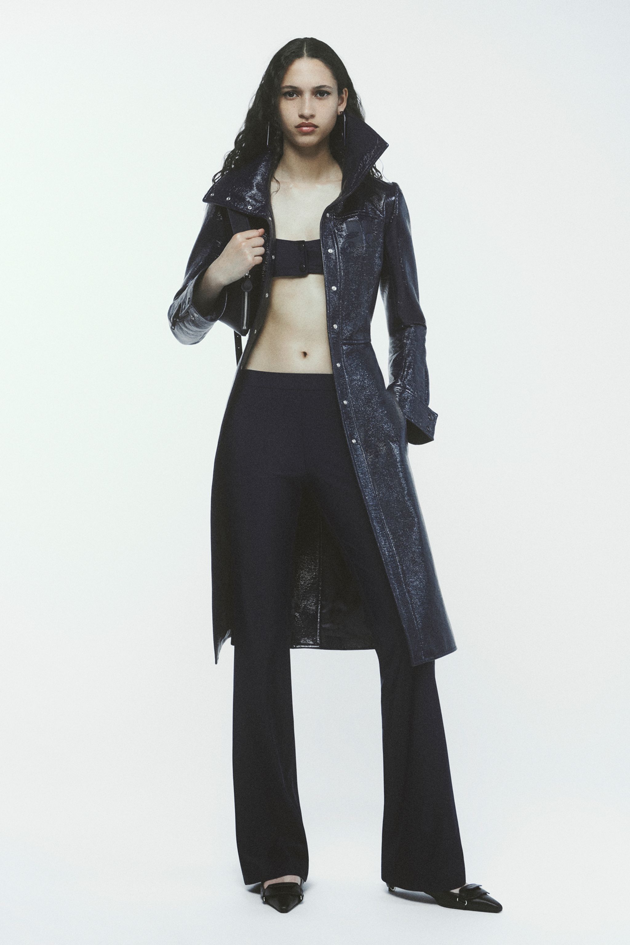 Elegant model in dark trench coat and chic black pants on a white background for Courrèges.