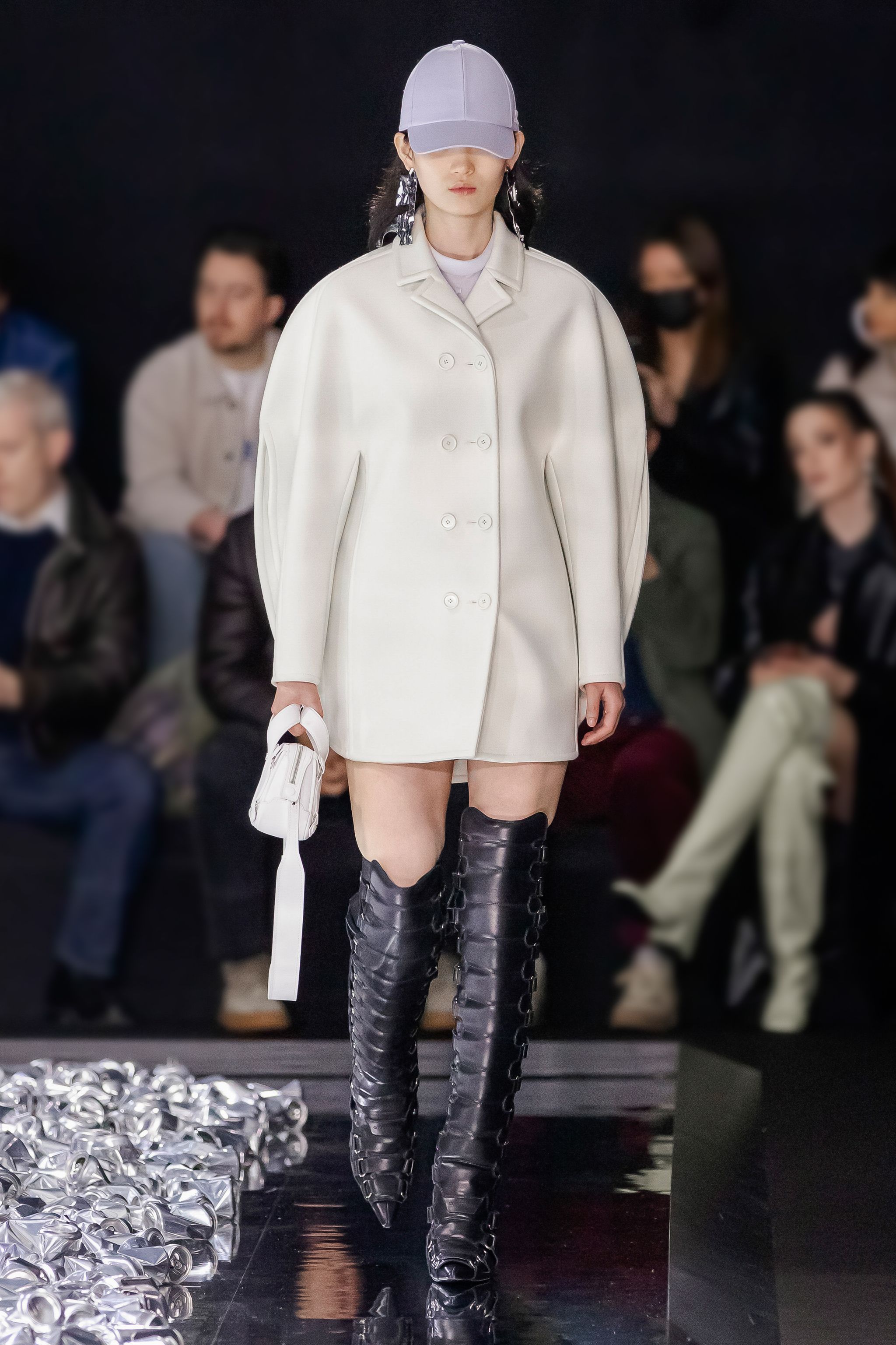 Elegant Courrèges runway model in a white coat, black thigh-high boots, and sporty cap.
