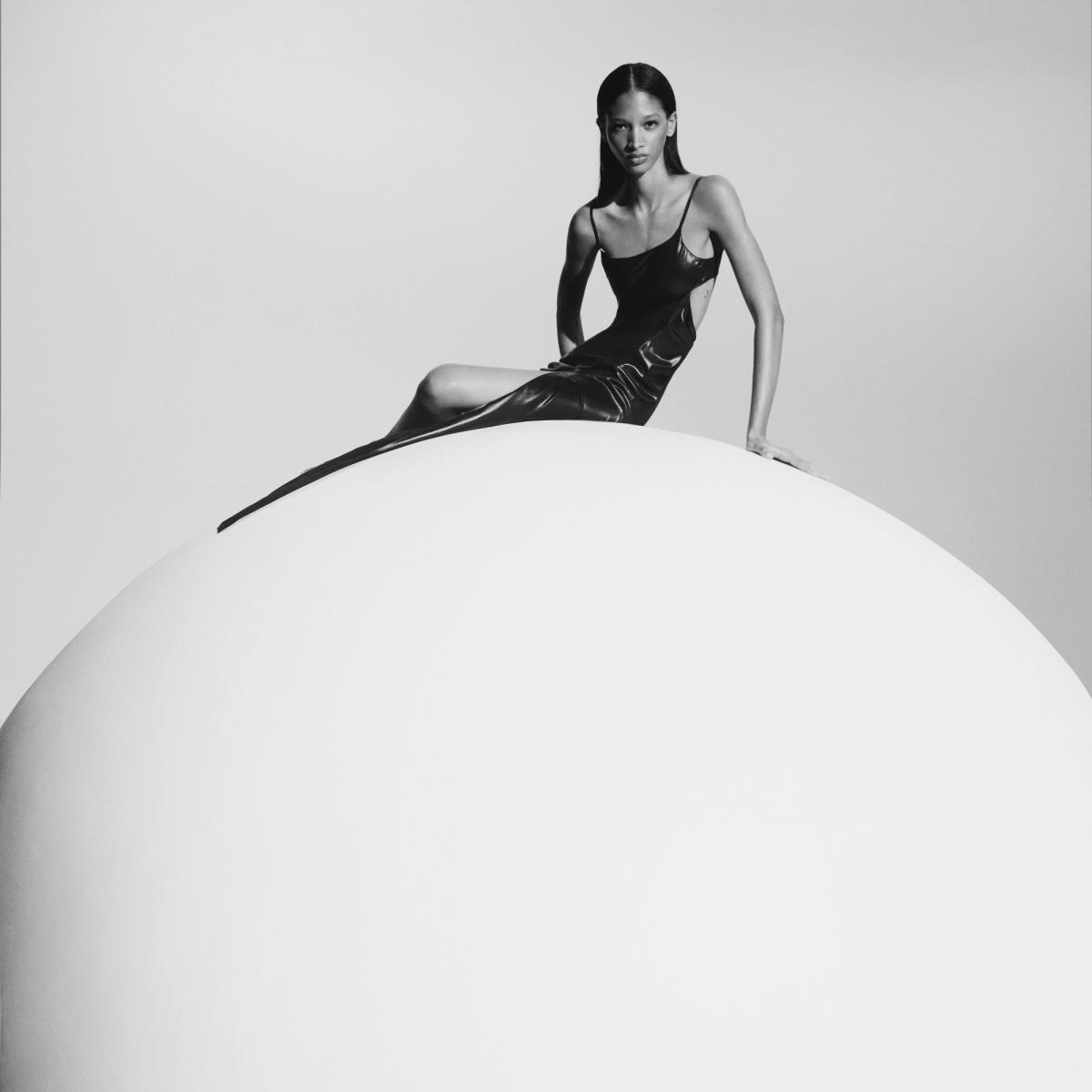 Elegant black dress by Courrèges on a model sitting on a minimalist spherical prop.