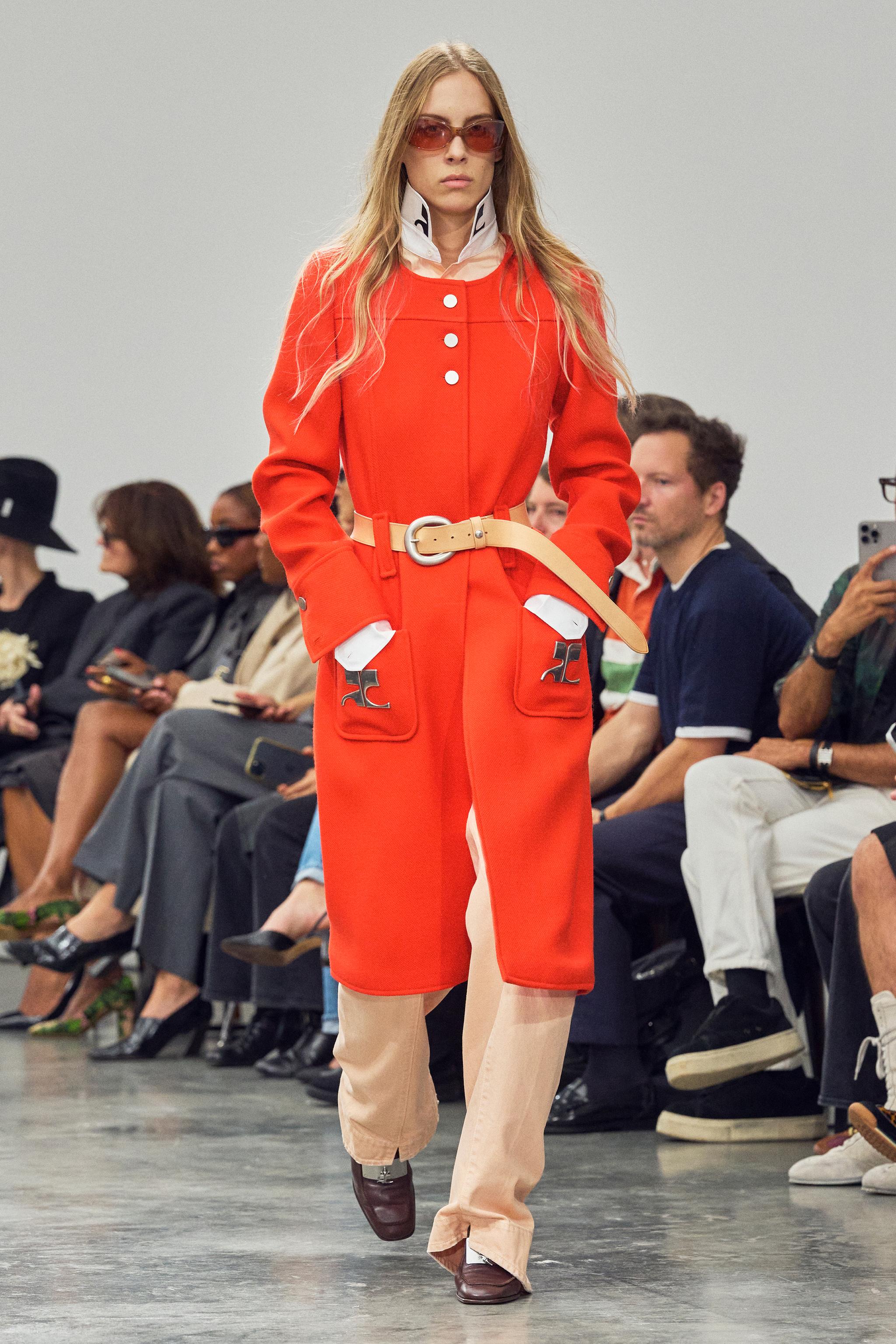 Elegant model walking runway in vibrant red jacket by Courrèges on fashion show.