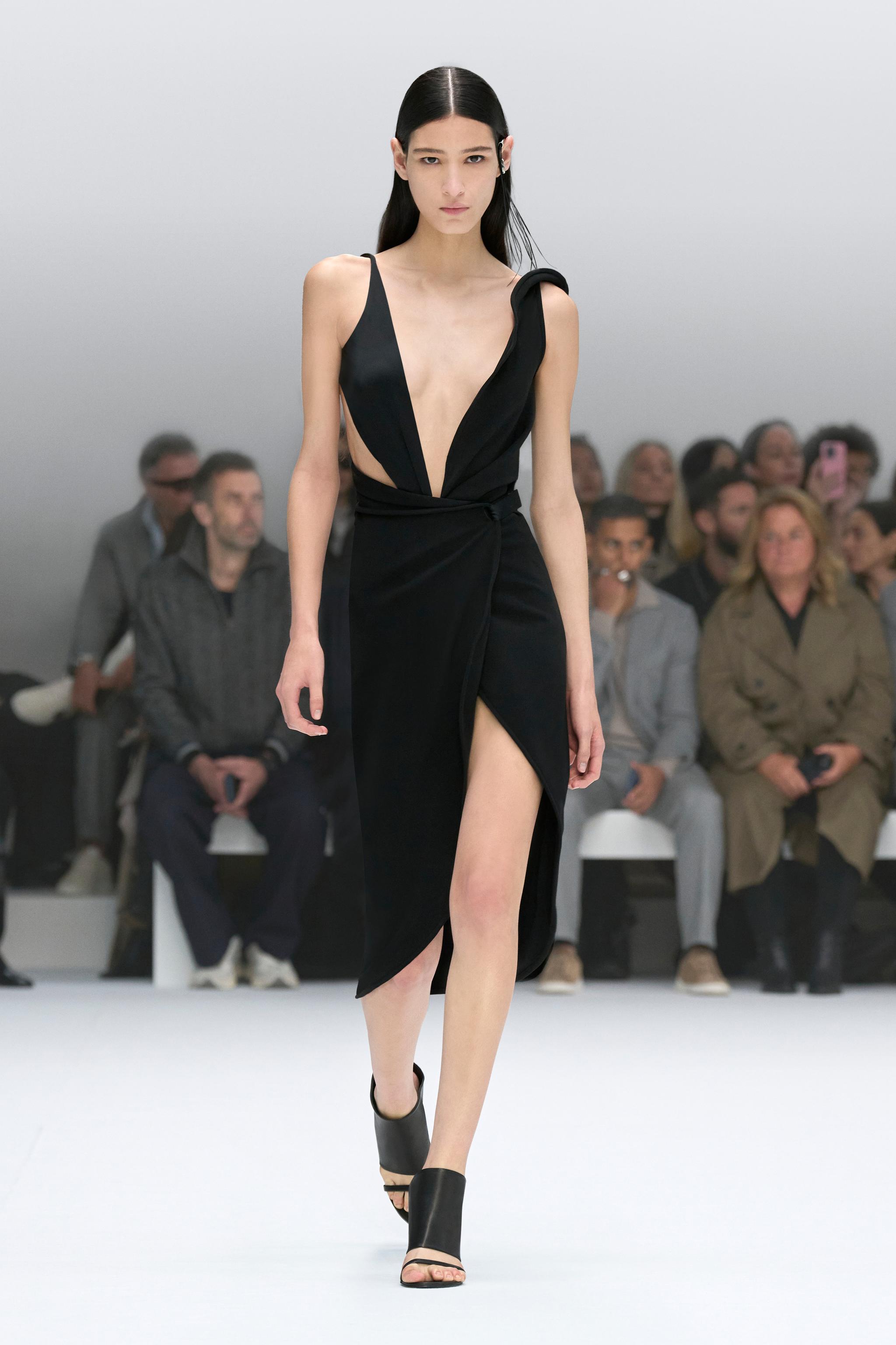 Elegant black dress with a plunging neckline and high slit, showcased on a runway for Courrèges.