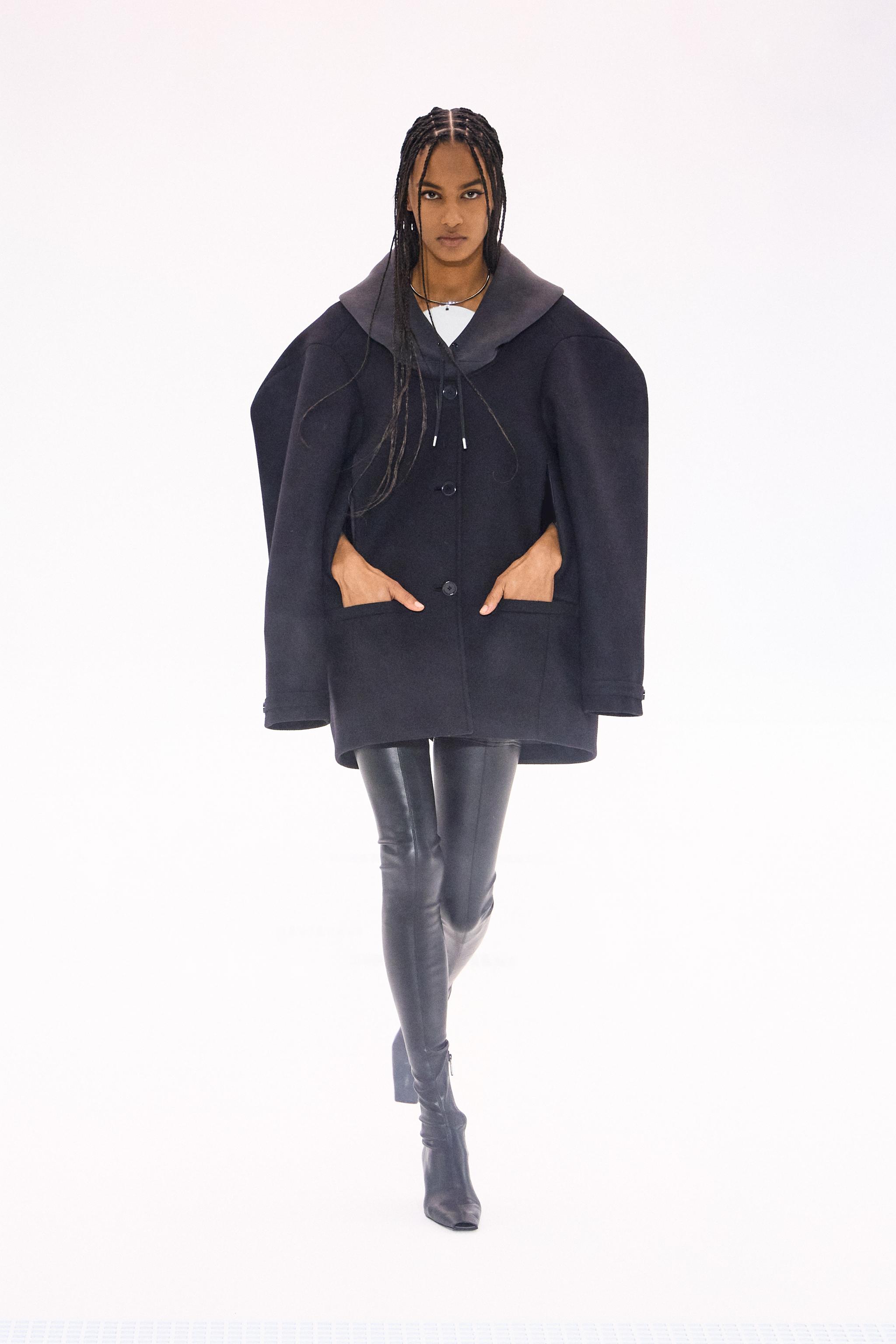 Elegant model showcasing Courrèges fashion with a black coat, leather leggings, and modern style.