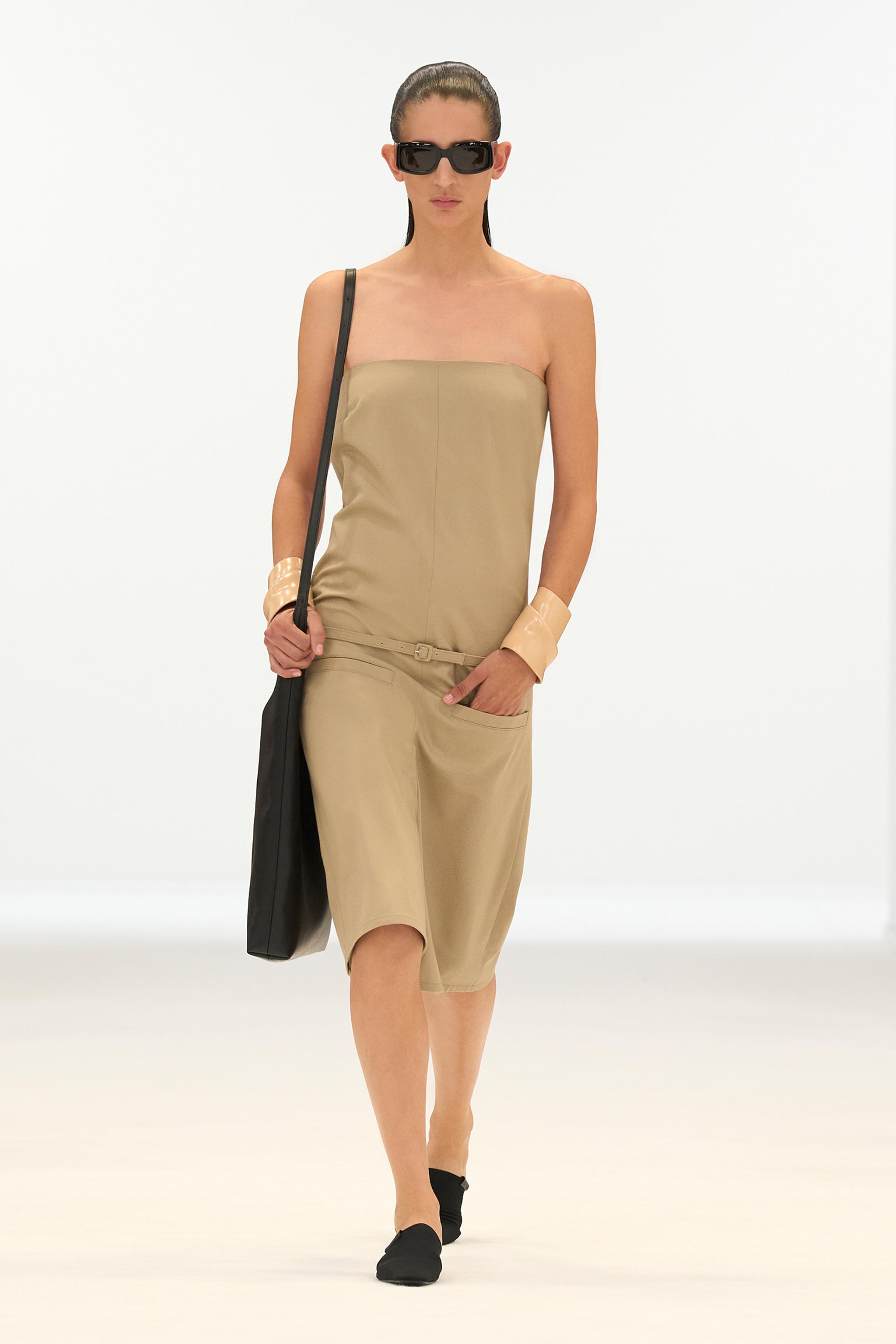 Elegant beige strapless dress by Courrèges, styled with black accessories on a runway.