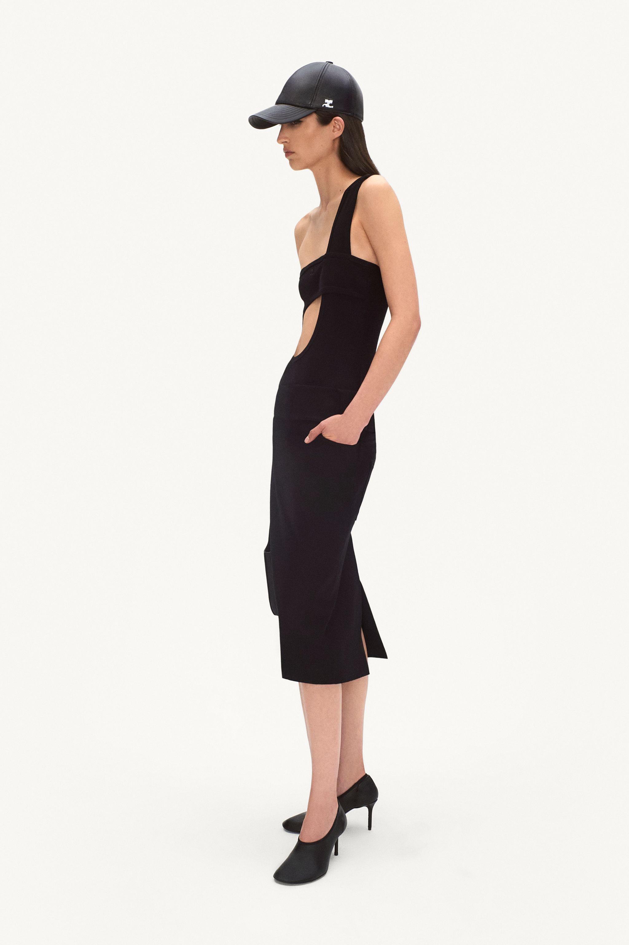 Elegant black Courrèges dress with cutouts, paired with heels and a cap for fashion-forward style.