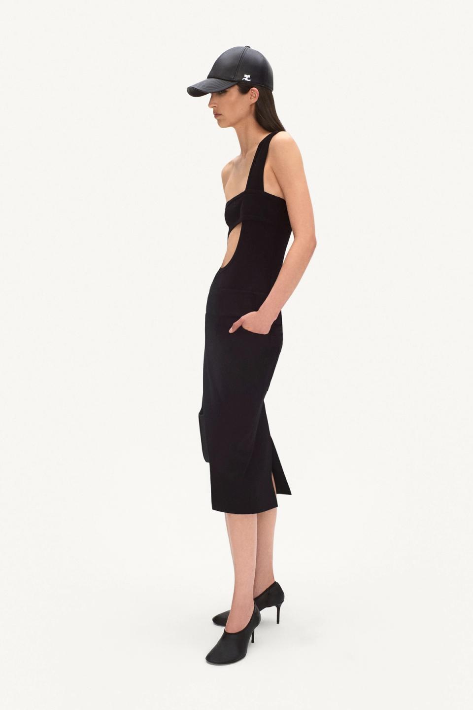 Elegant black Courrèges dress with cutouts, paired with heels and a cap for fashion-forward style.