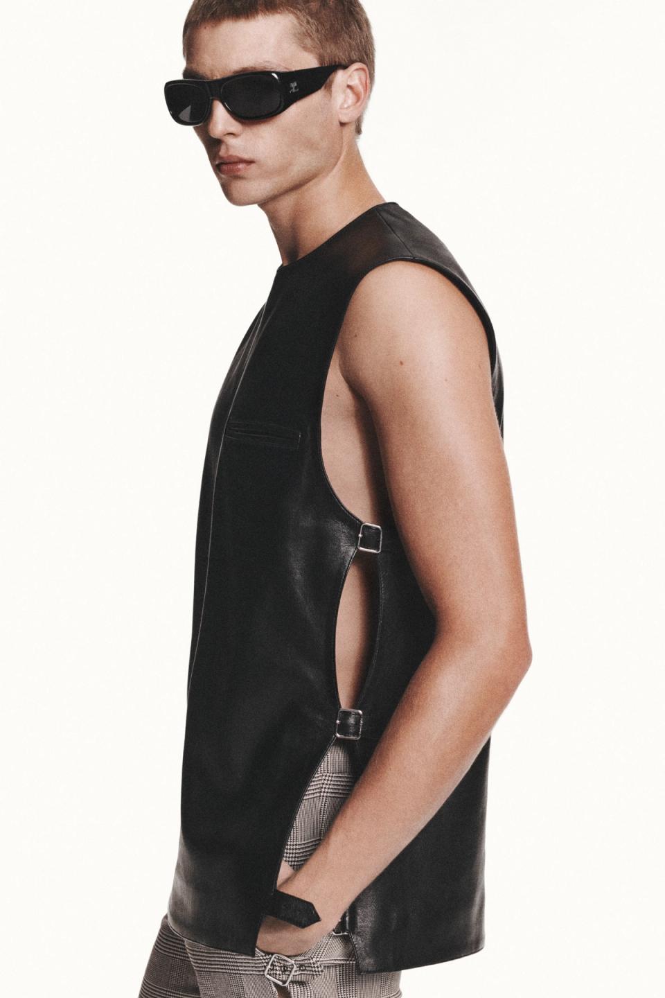 Elegant black sleeveless leather vest with buckle details, model with sunglasses for Courrèges.