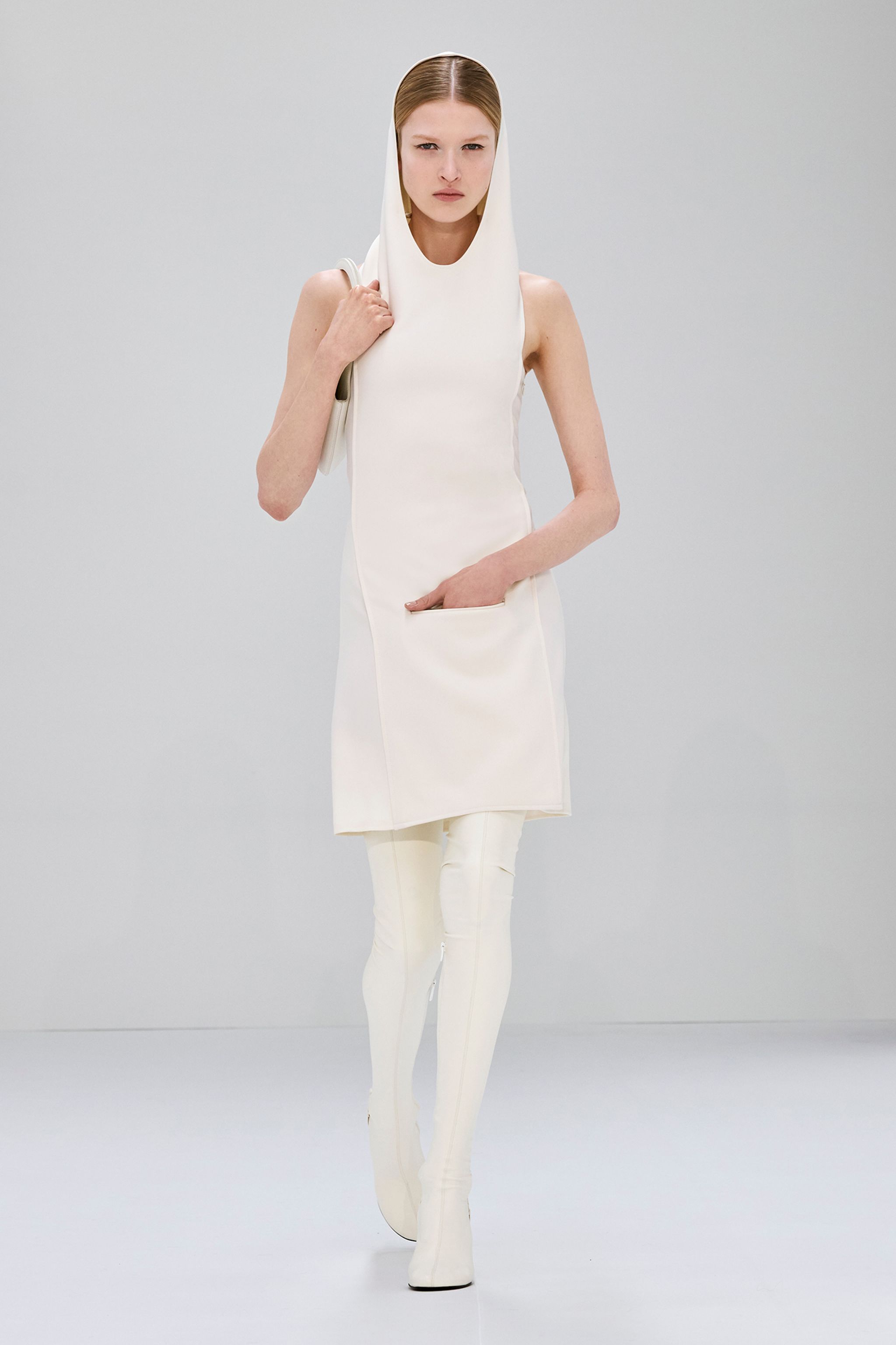 Elegant white dress and thigh-high boots from Courrèges showcased on a runway model.